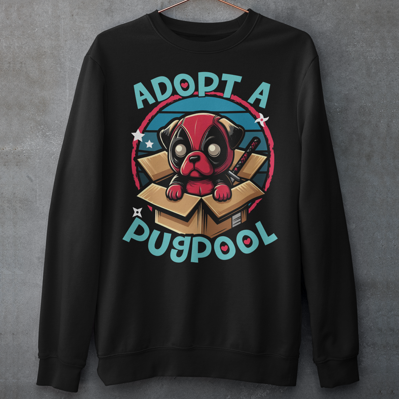 The Sweatshirt design features an adorable pug dressed as a mercenary, complete with a tiny red and black costume and a mask, sitting comfortably inside a slightly worn cardboard box. Around the design says "ADOPT A PUGPOOL" in a playful, hand-drawn font, giving it a quirky, homemade look.