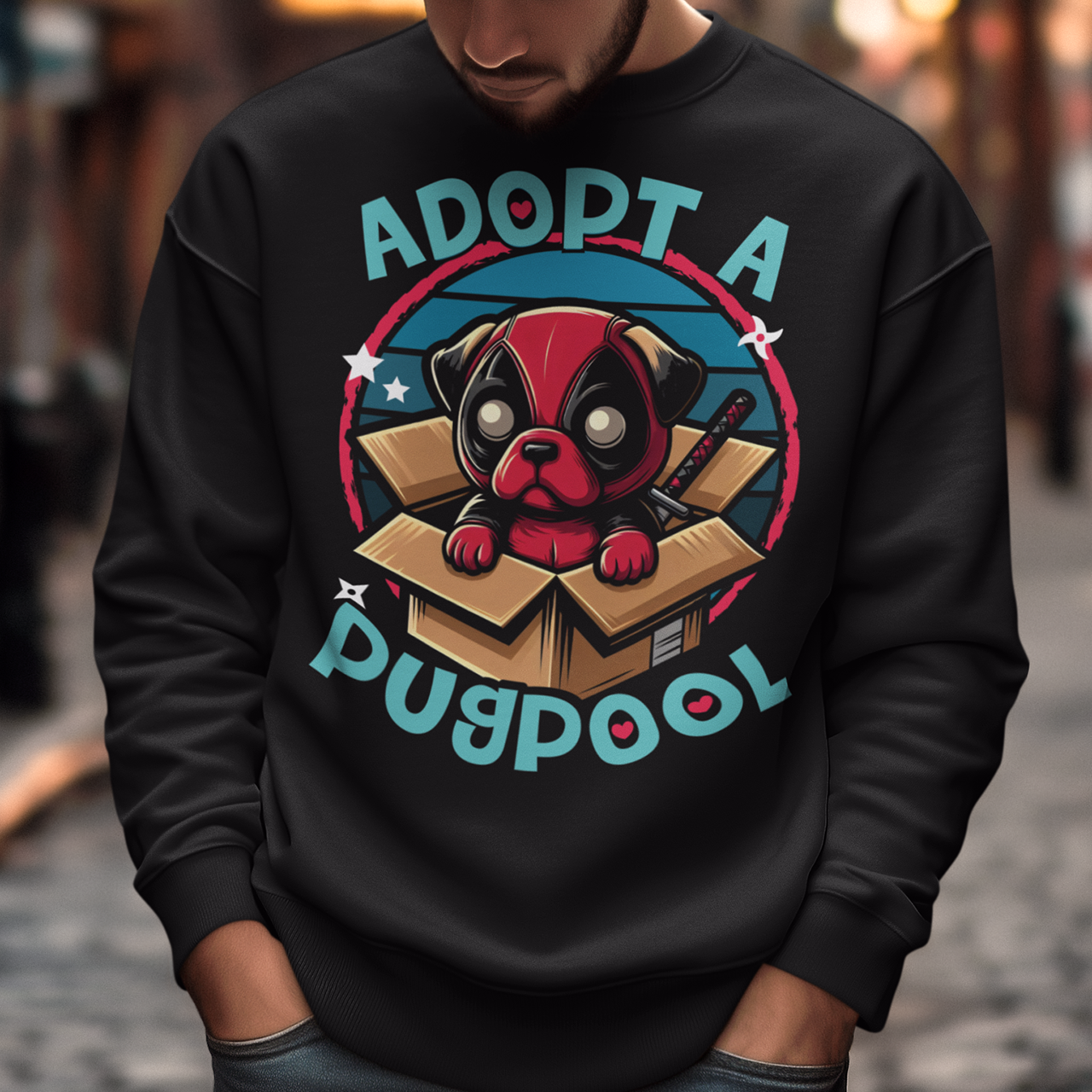 The Sweatshirt design features an adorable pug dressed as a mercenary, complete with a tiny red and black costume and a mask, sitting comfortably inside a slightly worn cardboard box. Around the design says "ADOPT A PUGPOOL" in a playful, hand-drawn font, giving it a quirky, homemade look.