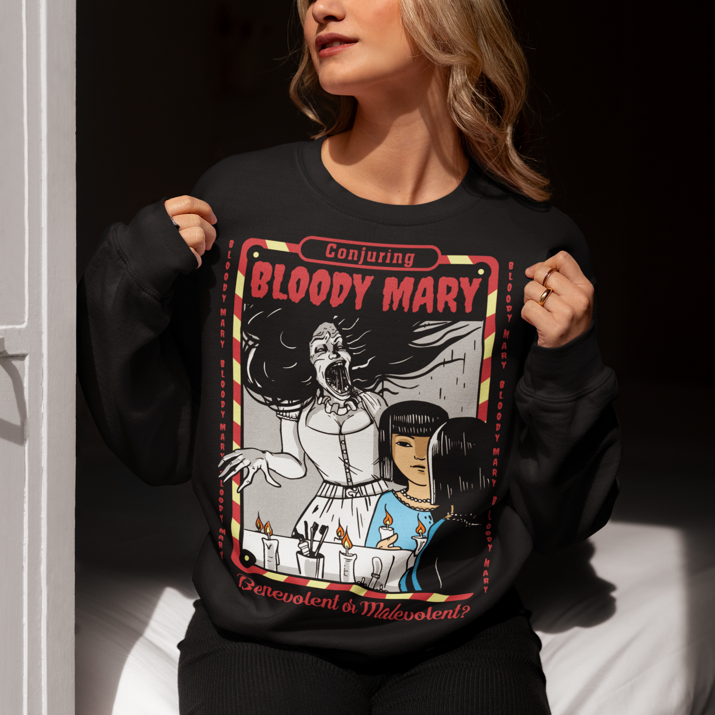 Dare to look twice. This chilling sweatshirt features a haunting design of a girl staring into a mirror—only to find Bloody Mary staring back from the reflection. Above, the bold words “Conjuring Bloody Mary” summon the legend, while below, the question “Benevolent or malevolent?” dares the viewer to decide. This shirt is perfect for horror fans, urban legend lovers, and anyone who enjoys walking the line between myth and reality.
