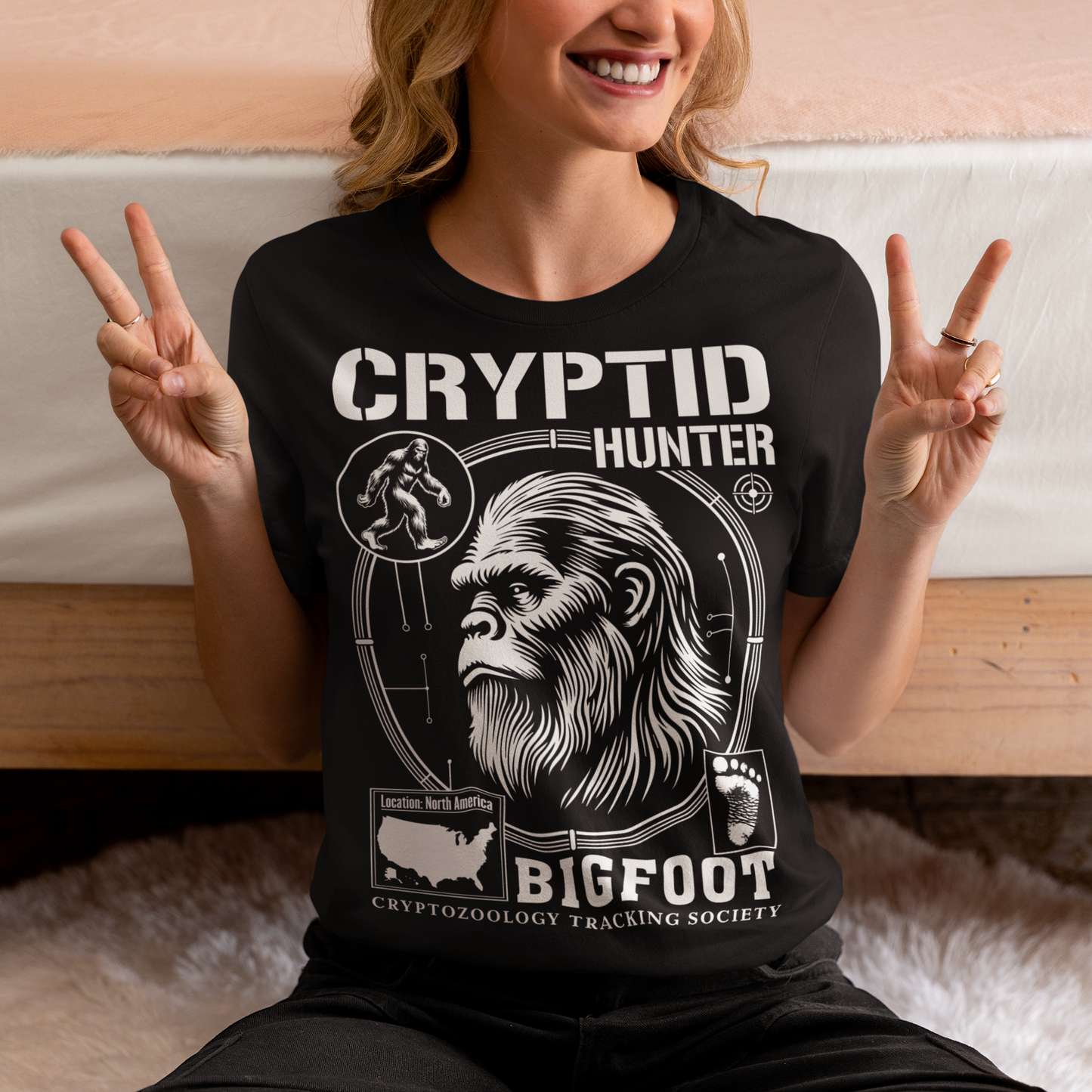 Illustration of a cryptozoology-themed t-shirt featuring a stylized image of Bigfoot's head, shown with shaggy fur, deep-set eyes, and a mysterious expression. The artwork has a bold, rugged design in earthy tones, emphasizing the mythical nature of the creature. Above the image, the words "CRYPTID HUNTER" are prominently displayed in large, distressed lettering, suggesting adventure and mystery. The design appeals to fans of folklore, legends, and unexplained phenomena.