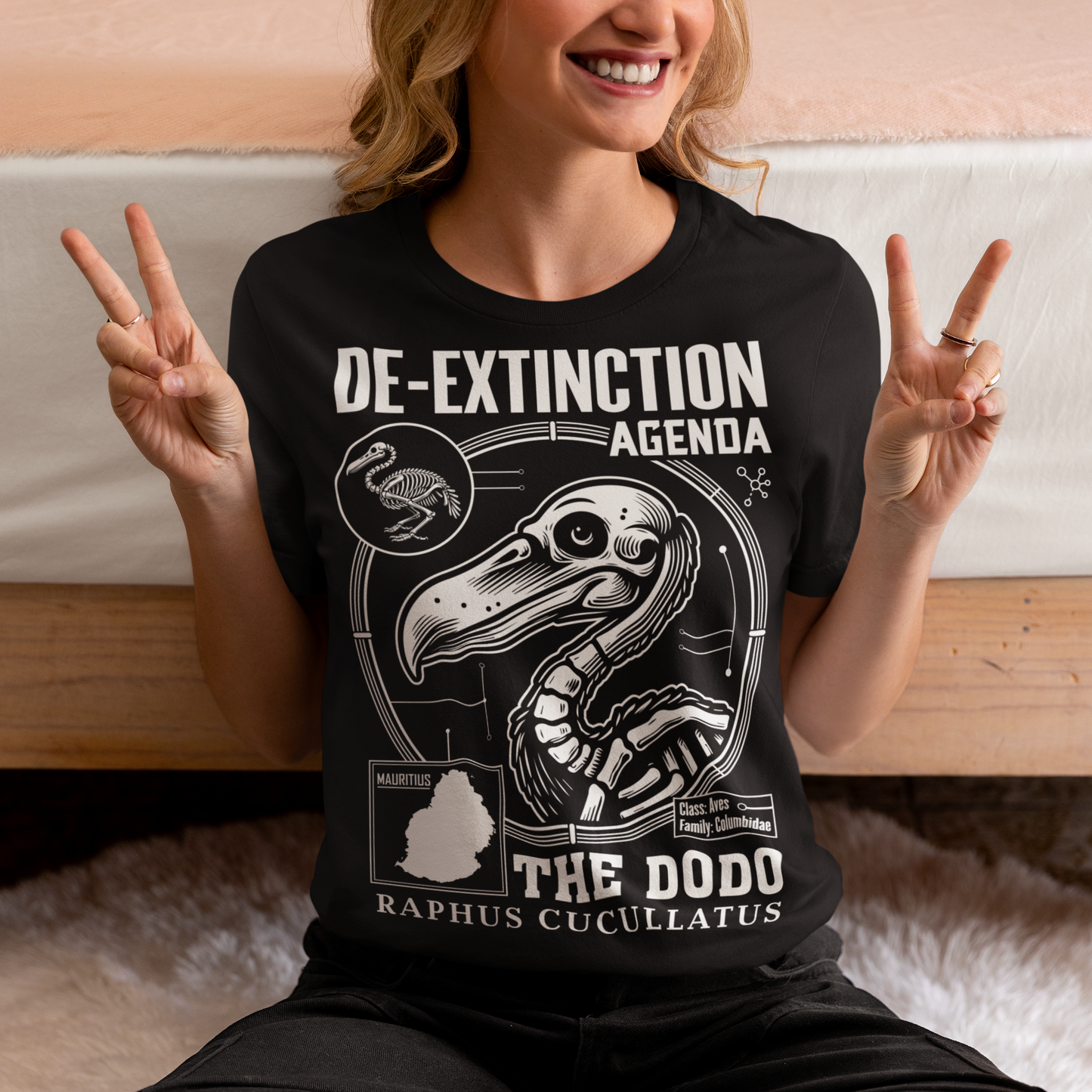 A graphic t-shirt featuring a stylized cartoon illustration of a dodo bird standing proudly with a determined expression. Above the dodo, bold, futuristic text reads “DE-EXTINCTION AGENDA.” The design combines retro and sci-fi elements, suggesting a revival or futuristic mission to bring the extinct bird back to life. The shirt uses vibrant colors and dynamic lines to create a playful yet rebellious aesthetic, appealing to fans of science, nature, or quirky fashion.