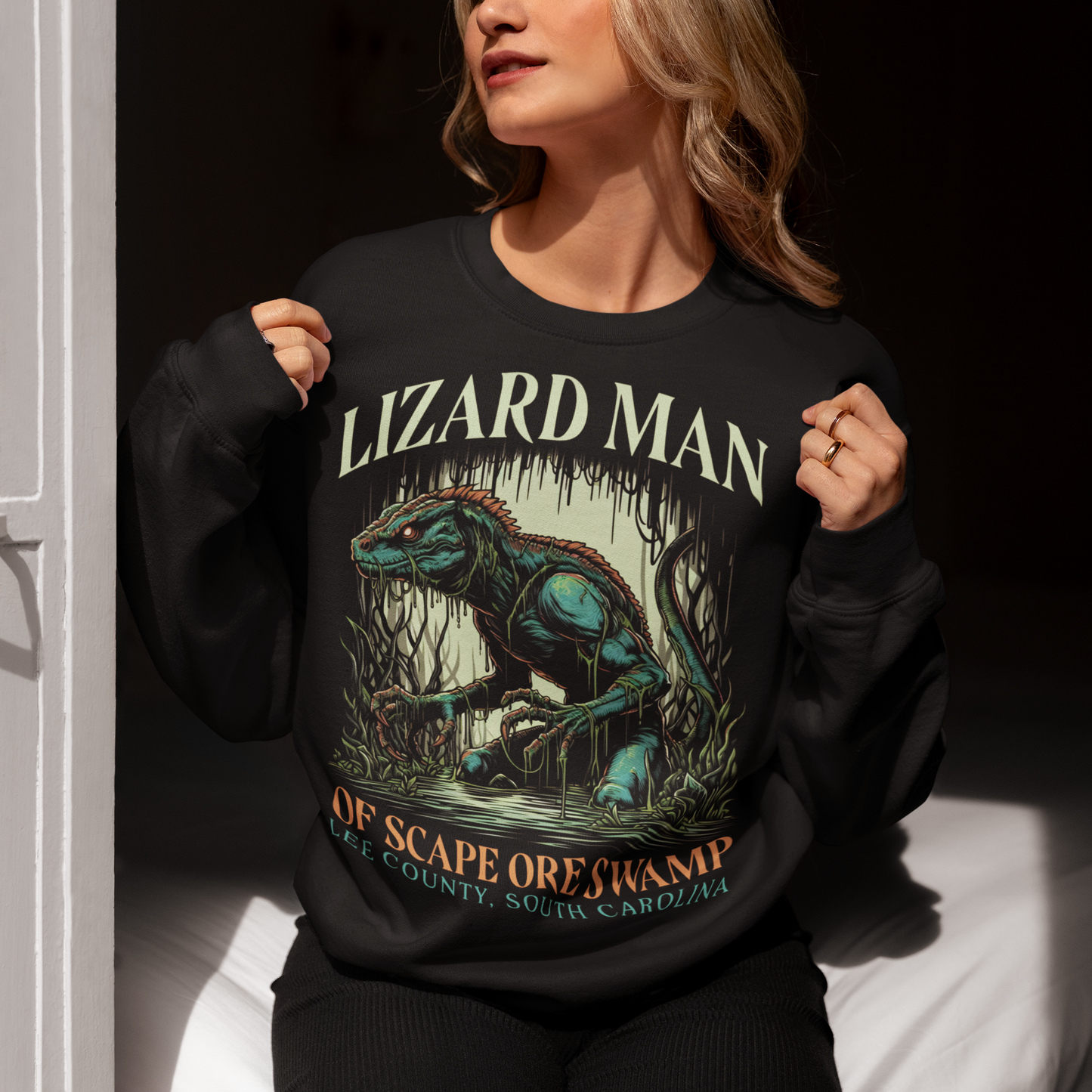 This sweatshirt features a striking design of the legendary "Lizard Man of Scape Ore Swamp." The centerpiece is a menacing yet intriguing lizard man emerging from the murky depths of a swamp, with reptilian scales glistening under the eerie moonlight. The creature's glowing yellow eyes peer out from beneath a rugged brow, and its powerful claws grasp at the twisted roots and moss that surround it.