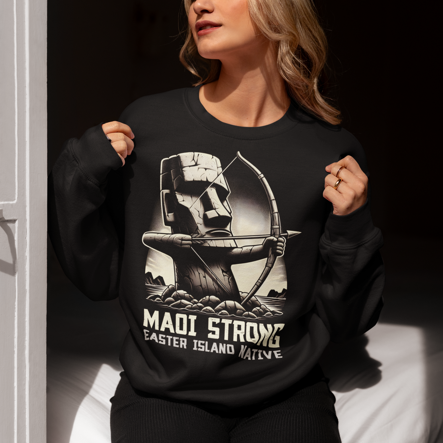This bold sweatshirt design features a dynamic illustration of a Moai statue, iconic to Easter Island, standing tall and proud. The Moai is depicted holding a bow and arrow, symbolizing strength and resilience. The statue is detailed with strong, angular lines and stone textures, giving it an authentic yet artistic appearance. Beneath the striking image, the text reads in bold, capitalized letters: "MAOI STRONG EASTER ISLAND NATIVE."