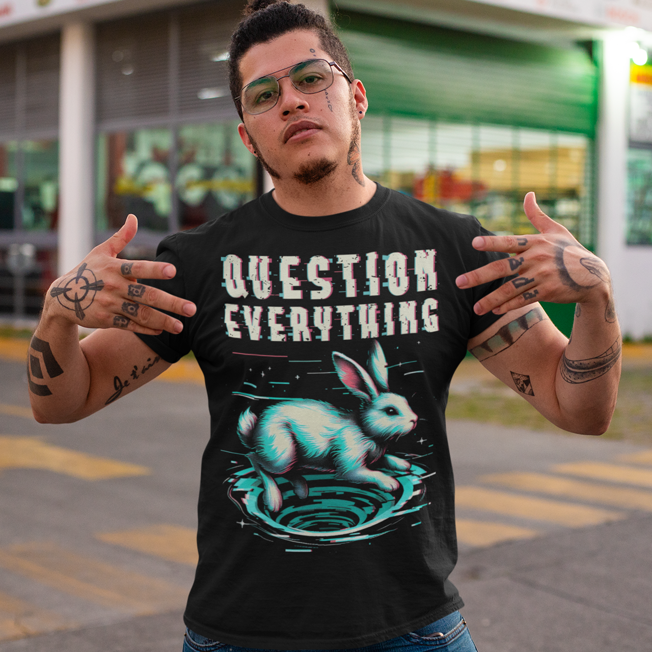 A graphic t-shirt featuring a stylized illustration of a white rabbit diving headfirst into a swirling rabbit hole. The rabbit's legs and tail are visible as it disappears into the tunnel, surrounded by abstract, distorted digital effects. Above the image, the phrase "QUESTION EVERYTHING" appears in bold, glitched typography, as if corrupted or scrambled, adding a sense of mystery and rebellion. The design evokes curiosity and themes of exploration and truth-seeking.