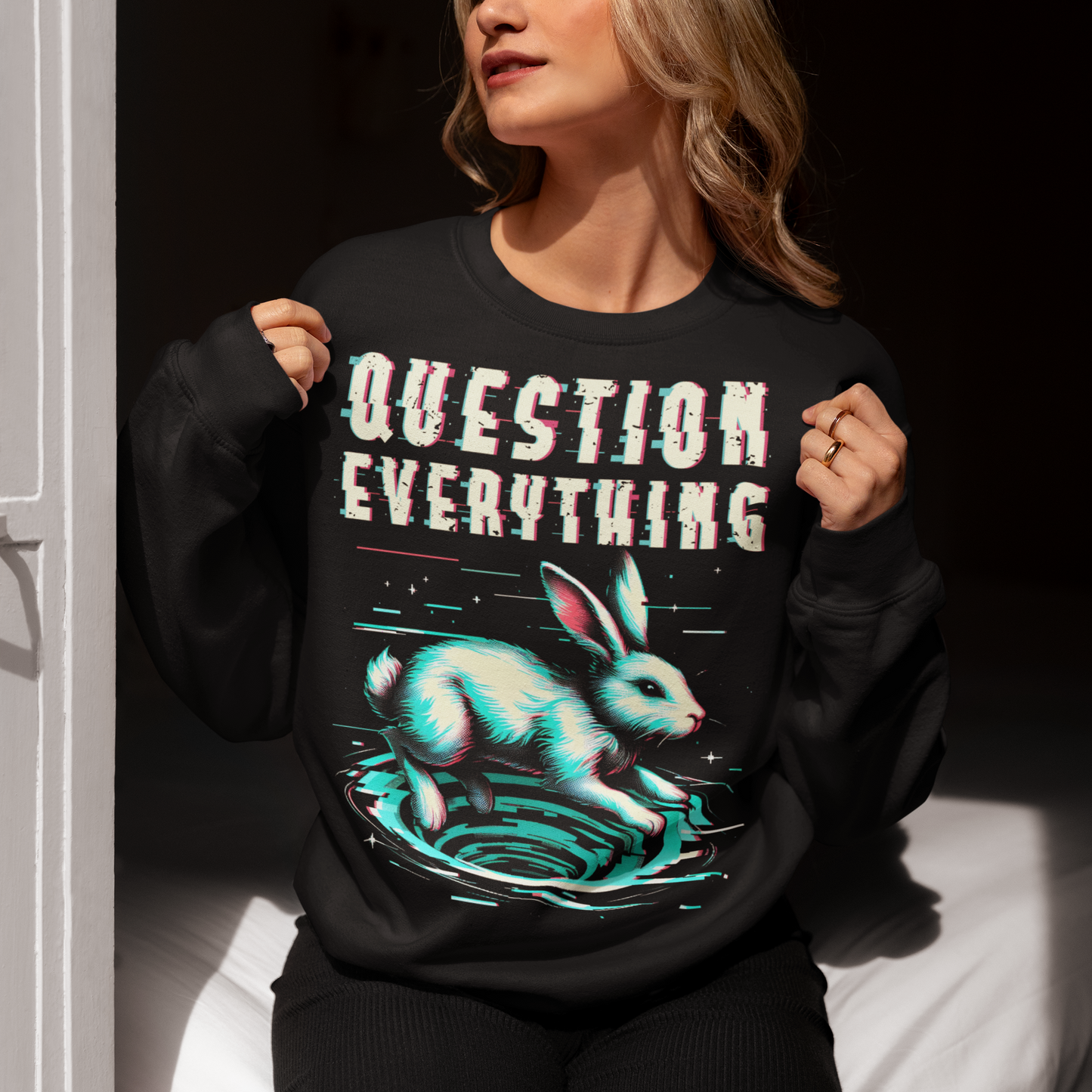 A graphic sweatshirt featuring a stylized illustration of a white rabbit diving headfirst into a swirling rabbit hole. The rabbit's legs and tail are visible as it disappears into the tunnel, surrounded by abstract, distorted digital effects. Above the image, the phrase "QUESTION EVERYTHING" appears in bold, glitched typography, as if corrupted or scrambled, adding a sense of mystery and rebellion. The design evokes curiosity and themes of exploration and truth-seeking.