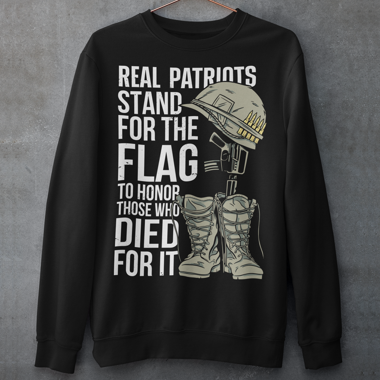 Sweatshirt design featuring a graphic of a military helmet resting on a rifle, which is standing upright in a pair of combat boots—a battlefield cross symbolizing fallen soldiers. Above and below the image is bold text that reads: "REAL PATRIOTS STAND FOR THE FLAG TO HONOR THOSE WHO DIED FOR IT." The design uses patriotic imagery to emphasize respect and remembrance for military service members who have sacrificed their lives.
