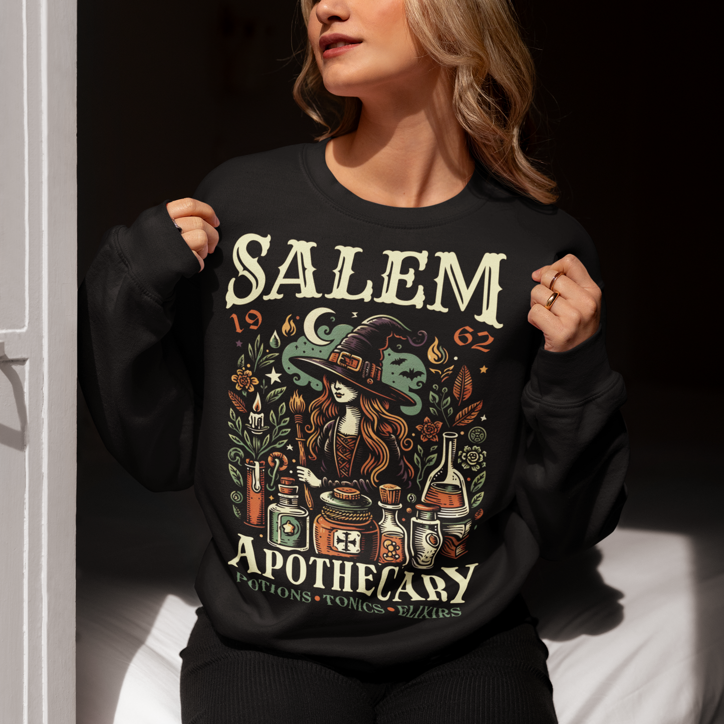 Step into the mystique of Salem with our "Salem Apothecary" Sweatshirt, a perfect blend of witchy charm and vintage flair. This design features a captivating witch, dressed in traditional attire, brewing potions with an array of mystical bottles and herbs. On the design the words "SALEM APOTHECARY" are prominently displayed, evoking the enchanting atmosphere of an old-world potion shop. This shirt is ideal for those who love the allure of witchcraft and the history of Salem.