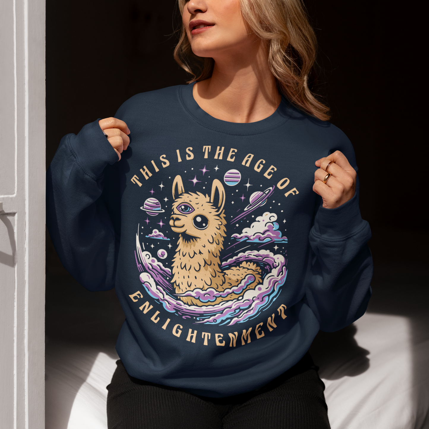 Embrace cosmic wisdom with our captivating Llama sweatshirt! Picture this: amidst the vast expanse of space, a serene Llama gazes into the universe, its third eye gleaming with enlightenment. With swirling galaxies as its backdrop, this design captures the essence of transcendence and insight. Around the celestial spectacle, bold text declares, 'THIS IS THE AGE OF ENLIGHTENMENT,' heralding a new era of awareness and understanding.