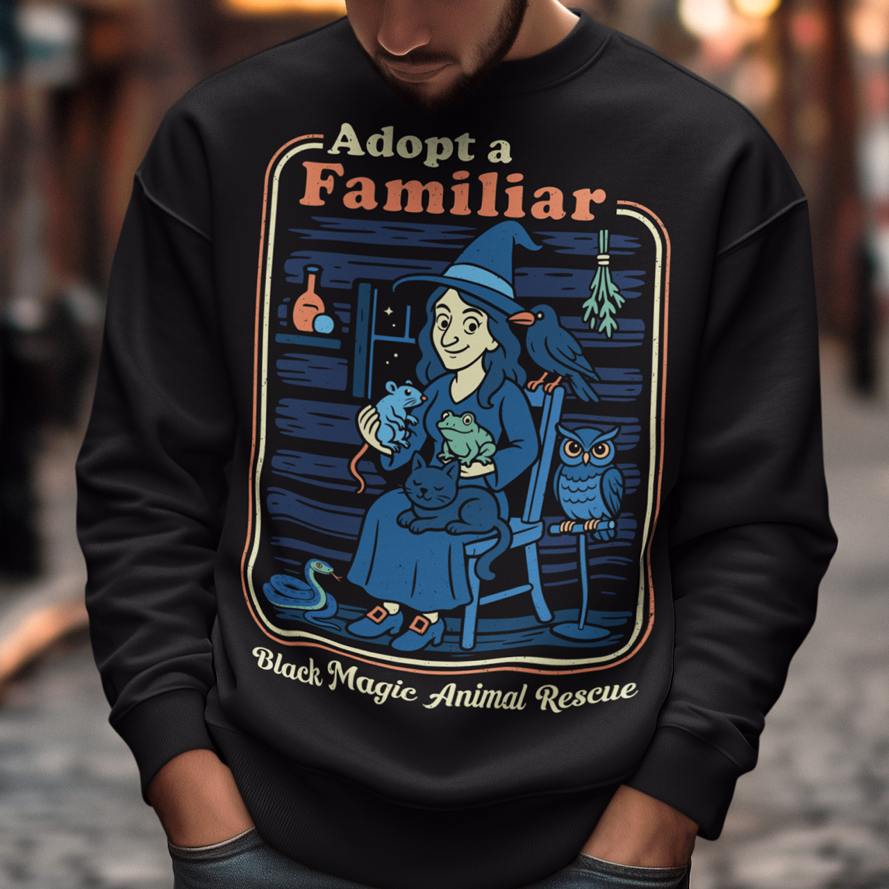 This cozy black sweatshirt features a charming illustration of a gentle witch surrounded by her rescued “familiars,” a cat curled in her lap, a curious frog, a loyal crow, a wise owl, and even a tiny snake slithering by. Framed like a vintage storybook scene, the design pairs warm, muted colors with playful linework and the heart-stealing phrase “Adopt a Familiar” above “Black Magic Animal Rescue. This shirt is perfect for animal lovers.