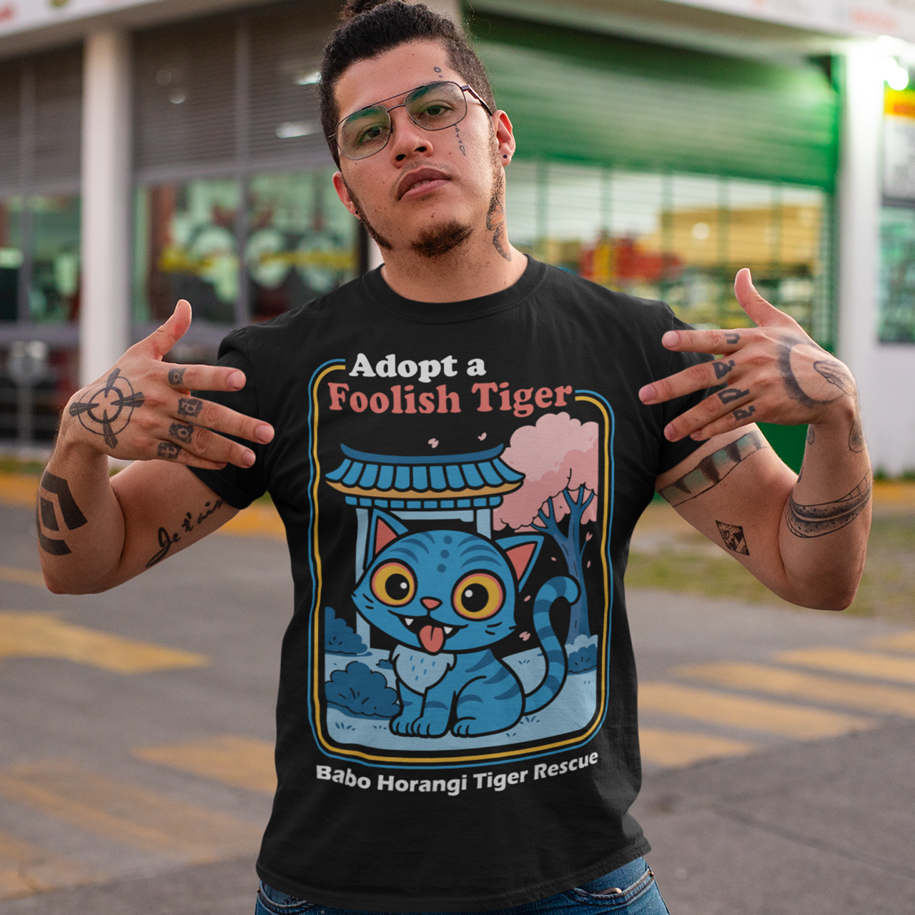 Adopt a foolish tiger t-shirt. Derpy kpop demon hunters shirt. Babo Horangi tee. This design feels like a Korean folklore creature wandered into a Saturday morning cartoon and decided to stay for snacks. A wide eyed blue “foolish tiger” sits under a temple gate with cherry blossoms drifting by, tongue out, zero survival instincts, maximum charm. The playful mix of myth inspired setting and goofy expression makes it equal parts legend and lovable disaster.on hunters shirt.