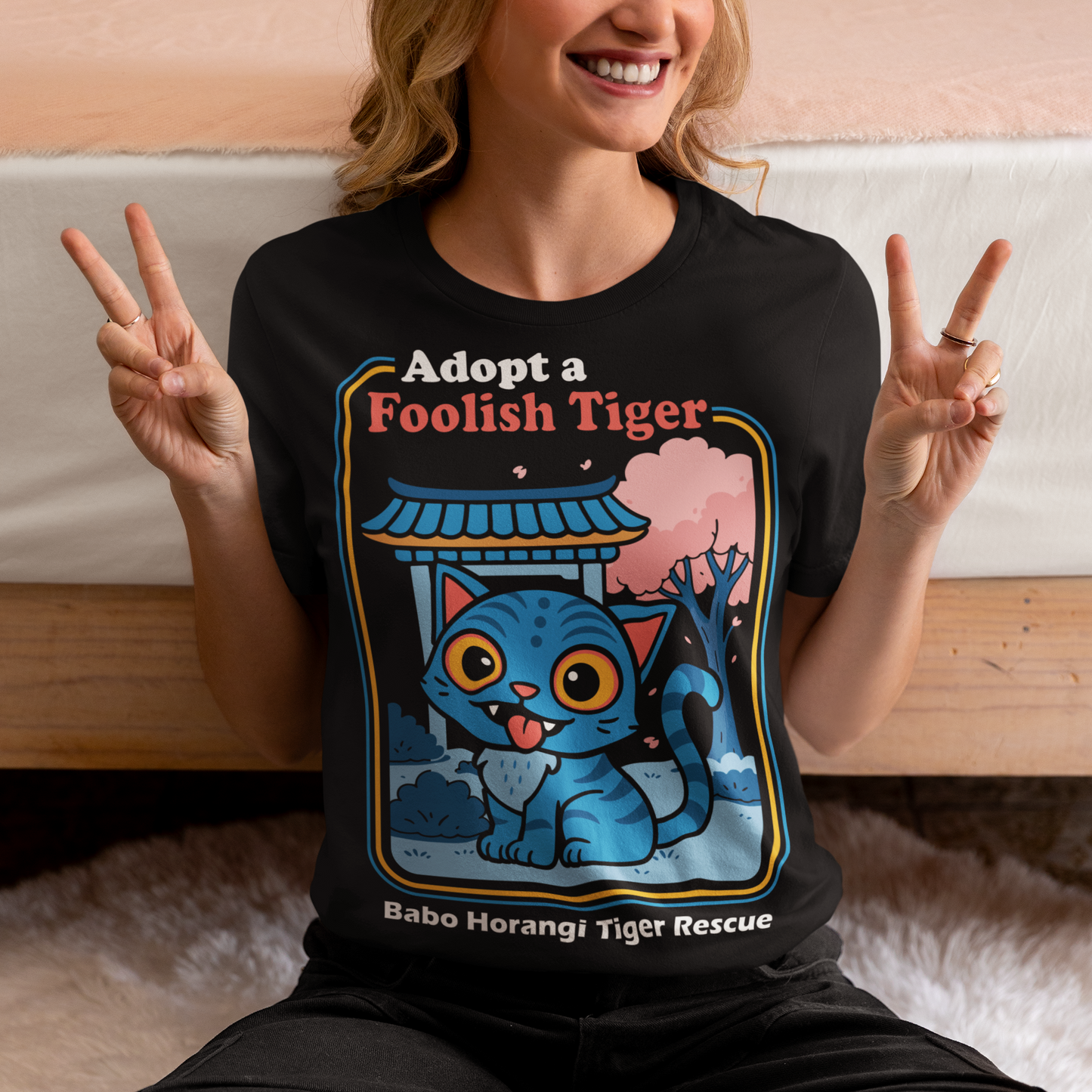 Adopt a foolish tiger t-shirt. Derpy kpop demon hunters shirt. Babo Horangi tee. This design feels like a Korean folklore creature wandered into a Saturday morning cartoon and decided to stay for snacks. A wide eyed blue “foolish tiger” sits under a temple gate with cherry blossoms drifting by, tongue out, zero survival instincts, maximum charm. The playful mix of myth inspired setting and goofy expression makes it equal parts legend and lovable disaster.on hunters shirt.