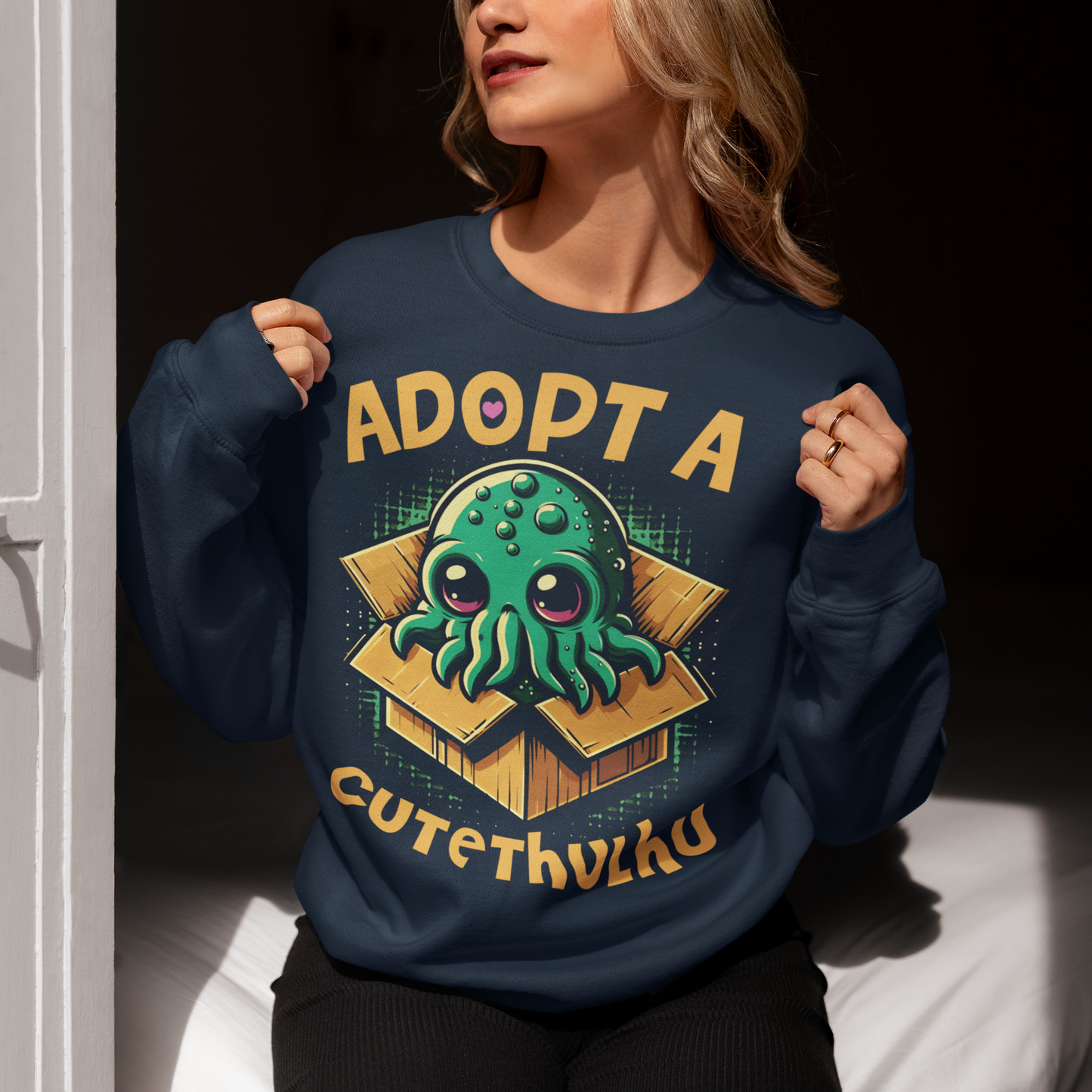 Navy sweatshirt of a cute Cthulhu in a cardboard box with text ADOPT A CUTETHULHU.