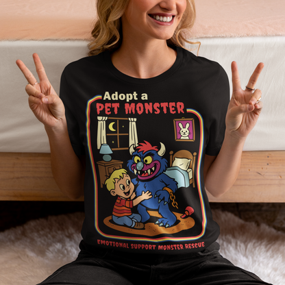 My pet monster t-shirt. Soft, spooky, and suspiciously adorable, this tee looks like it came straight from a slightly haunted Saturday morning cartoon vault. The design features a wide eyed kid befriending a fuzzy little monster with tiny horns and big attitude, all set inside a cozy bedroom scene with retro storybook vibes. The bold “Adopt a Pet Monster” headline and “Emotional Support Monster Rescue” tagline sell the joke perfectly, blending cute chaos with feel good humor.