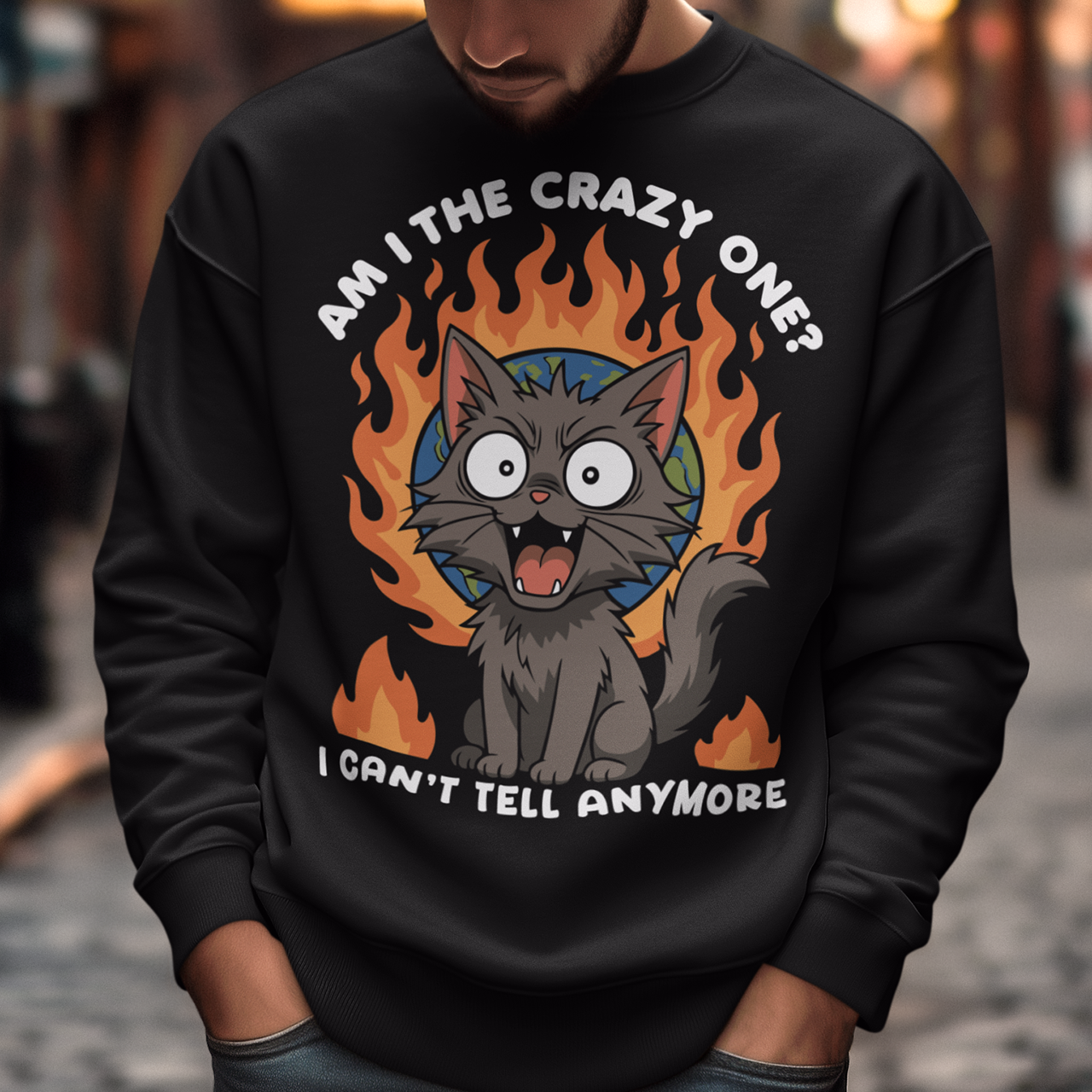 Black sweatshirt featuring a cartoon gray cat with wide eyes and sharp teeth, sitting in front of a flaming globe. The design includes the text “Am I the crazy one? I can’t tell anymore” in bold white letters. The illustration has a humorous, dark tone, combining chaotic energy with a cute yet slightly unhinged cat character.