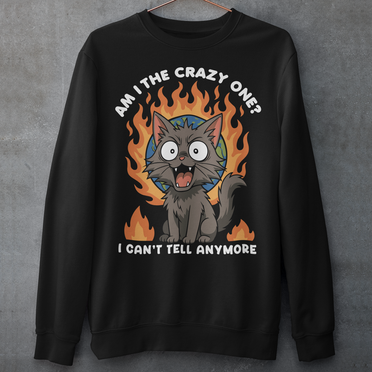 Black sweatshirt featuring a cartoon gray cat with wide eyes and sharp teeth, sitting in front of a flaming globe. The design includes the text “Am I the crazy one? I can’t tell anymore” in bold white letters. The illustration has a humorous, dark tone, combining chaotic energy with a cute yet slightly unhinged cat character.