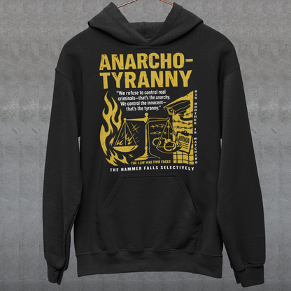 Black hoodie featuring a distressed yellow “ANARCHO-TYRANNY” graphic with scales of justice, flames, barbed wire, surveillance imagery, and prison-themed artwork. The design includes the phrases “THE LAW HAS TWO FACES” and “THE HAMMER FALLS SELECTIVELY,” creating a bold political statement focused on authority, government power, civil liberties, and anti-authoritarian themes.