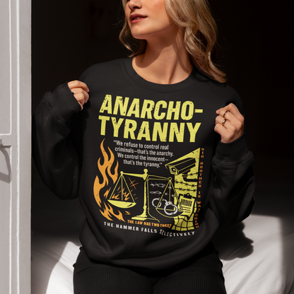 Black sweatshirt featuring a distressed yellow “ANARCHO-TYRANNY” graphic with scales of justice, flames, barbed wire, surveillance imagery, and prison-themed artwork. The design includes the phrases “THE LAW HAS TWO FACES” and “THE HAMMER FALLS SELECTIVELY,” creating a bold political statement focused on authority, government power, civil liberties, and anti-authoritarian themes.