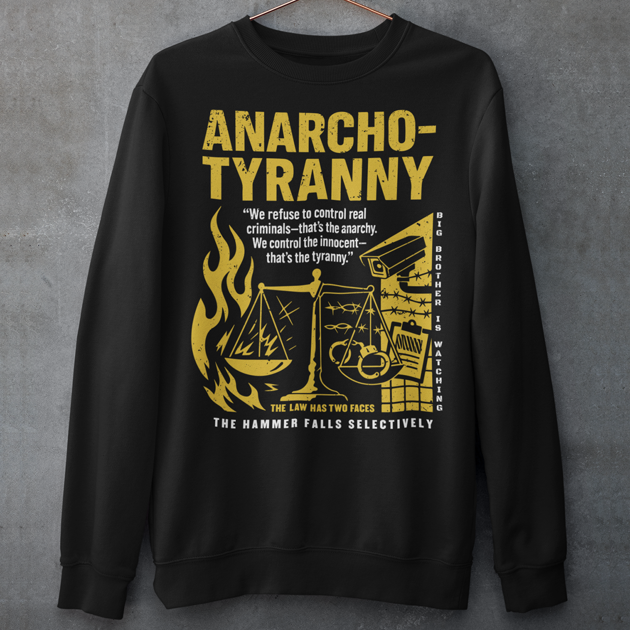 Black sweatshirt featuring a distressed yellow “ANARCHO-TYRANNY” graphic with scales of justice, flames, barbed wire, surveillance imagery, and prison-themed artwork. The design includes the phrases “THE LAW HAS TWO FACES” and “THE HAMMER FALLS SELECTIVELY,” creating a bold political statement focused on authority, government power, civil liberties, and anti-authoritarian themes.