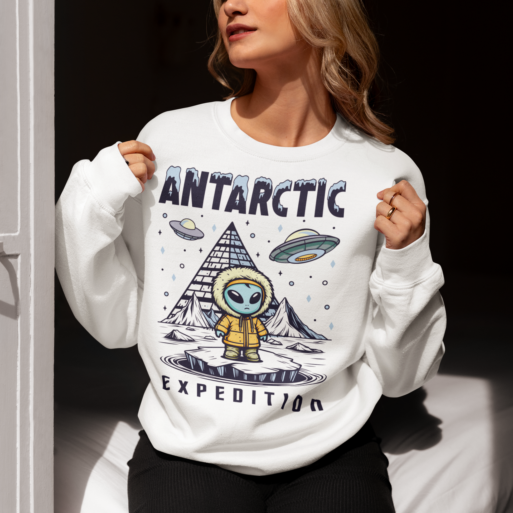 White sweatshirt of an Alien wearing a jacket in Antarctica with a pyramid in the background and UFOs in the sky with text ANTARCTIC EXPEDITION.