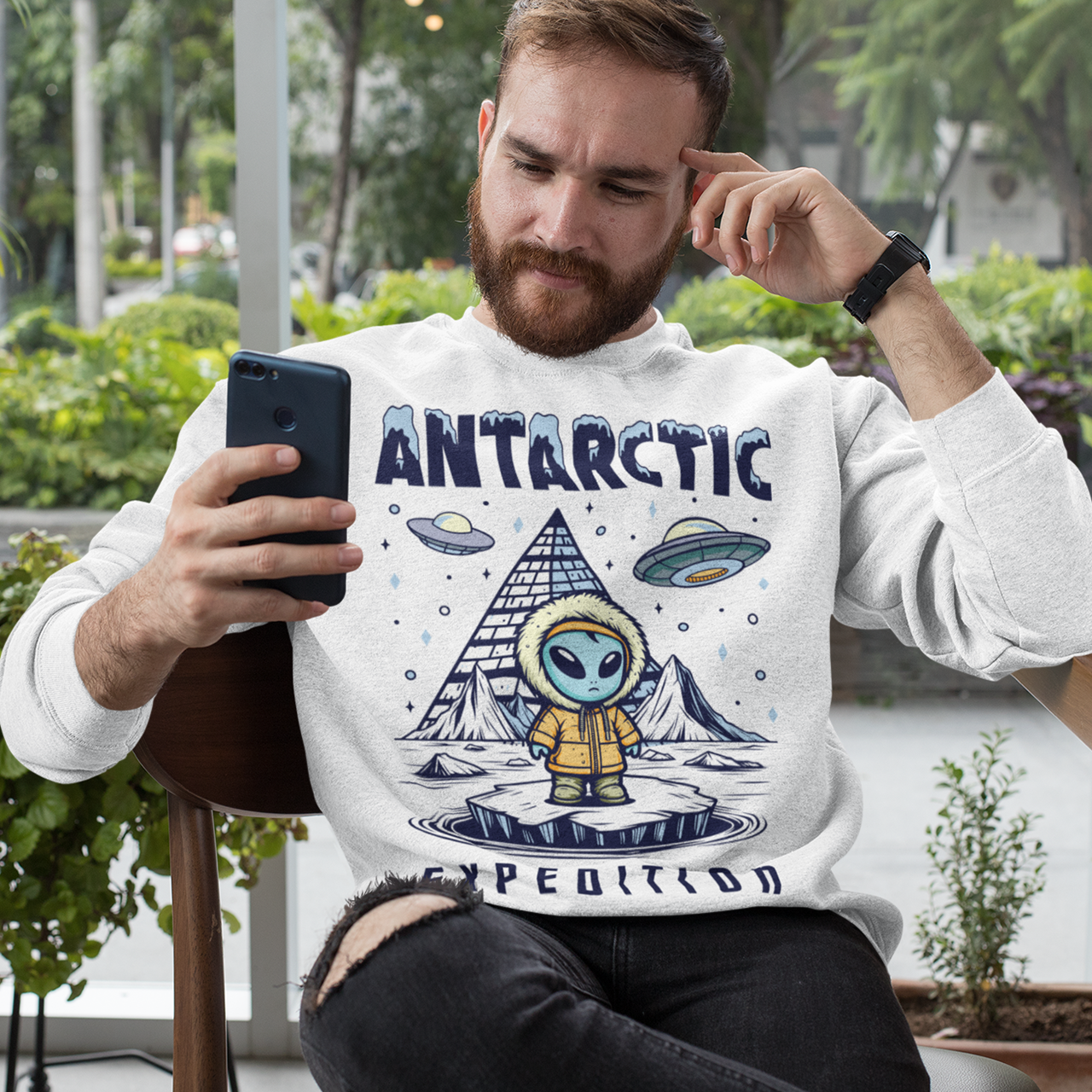 White sweatshirt of an Alien wearing a jacket in Antarctica with a pyramid in the background and UFOs in the sky with text ANTARCTIC EXPEDITION.