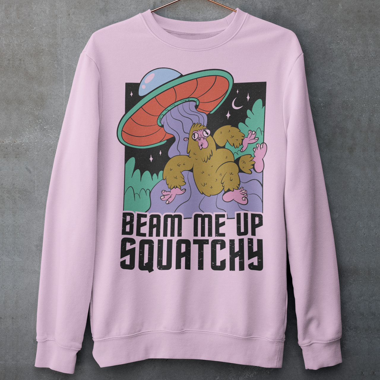 Pink sweatshirt of a sasquatch being abducted by a UFO with text BEAM ME UP SQUATCHY.