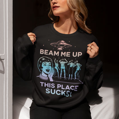 This snark-powered retro UFO sweatshirt brings the perfect escape fantasy to life. A vintage-style flying saucer hovers above a crowd while a wide-eyed woman rallies for interstellar rescue, paired with the bold line “Beam Me Up, This Place Sucks!” The design has a classic pulp-sci-fi look that feels like it tumbled out of an old comic rack. Ideal for anyone who survives their days with eye rolls, cosmic daydreams, and a desire to be anywhere else in the galaxy.