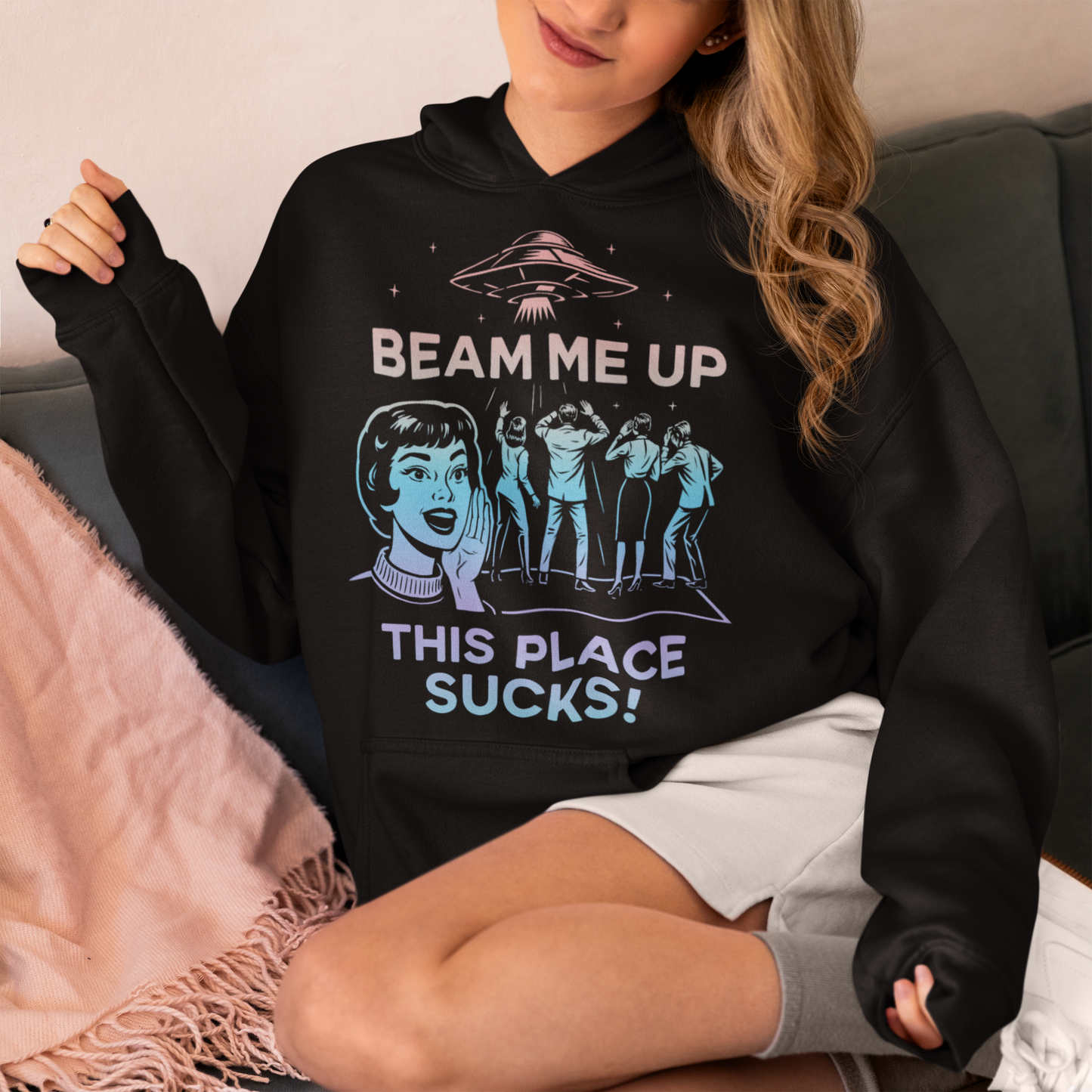 This snark-powered retro UFO hoodie brings the perfect escape fantasy to life. A vintage-style flying saucer hovers above a crowd while a wide-eyed woman rallies for interstellar rescue, paired with the bold line “Beam Me Up, This Place Sucks!” The design has a classic pulp-sci-fi look that feels like it tumbled out of an old comic rack. Ideal for anyone who survives their days with eye rolls, cosmic daydreams, and a desire to be anywhere else in the galaxy.