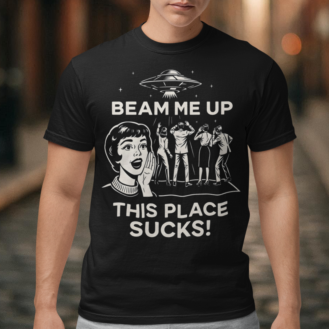 This snark-powered retro UFO t-shirt brings the perfect escape fantasy to life. A vintage-style flying saucer hovers above a crowd while a wide-eyed woman rallies for interstellar rescue, paired with the bold line “Beam Me Up, This Place Sucks!” The design has a classic pulp-sci-fi look that feels like it tumbled out of an old comic rack. Ideal for anyone who survives their days with eye rolls, cosmic daydreams, and a desire to be anywhere else in the galaxy.