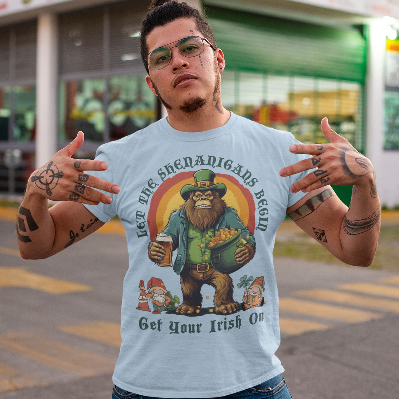 St Patrick's Day light blue t-shirt of a Bigfoot dressed as a leprechaun holding a beer and a pot of gold with text above LET THE SHENANIGANS BEGIN.