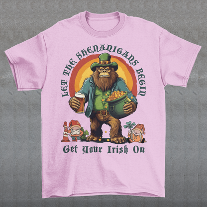 Get ready to celebrate St. Patrick's Day in style with our hilarious and festive Bigfoot-themed t-shirt! This shirt features everyone's favorite cryptid, Bigfoot, dressed in full leprechaun attire, complete with a green hat and shamrock-adorned vest. Bigfoot is depicted holding a frothy beer in one hand and a gleaming pot of gold in the other, ready to join in the festivities. Above this whimsical scene, bold text declares, "LET THE SHENANIGANS BEGIN."