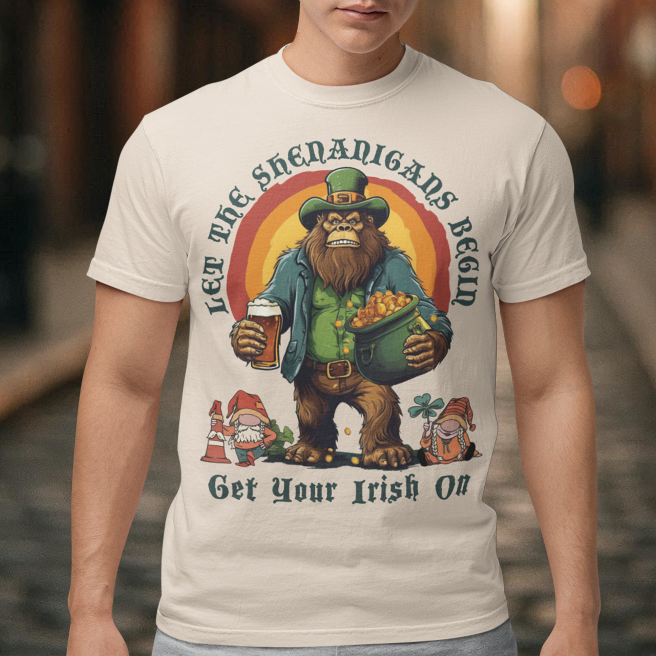 Get ready to celebrate St. Patrick's Day in style with our hilarious and festive Bigfoot-themed t-shirt! This shirt features everyone's favorite cryptid, Bigfoot, dressed in full leprechaun attire, complete with a green hat and shamrock-adorned vest. Bigfoot is depicted holding a frothy beer in one hand and a gleaming pot of gold in the other, ready to join in the festivities. Above this whimsical scene, bold text declares, "LET THE SHENANIGANS BEGIN."
