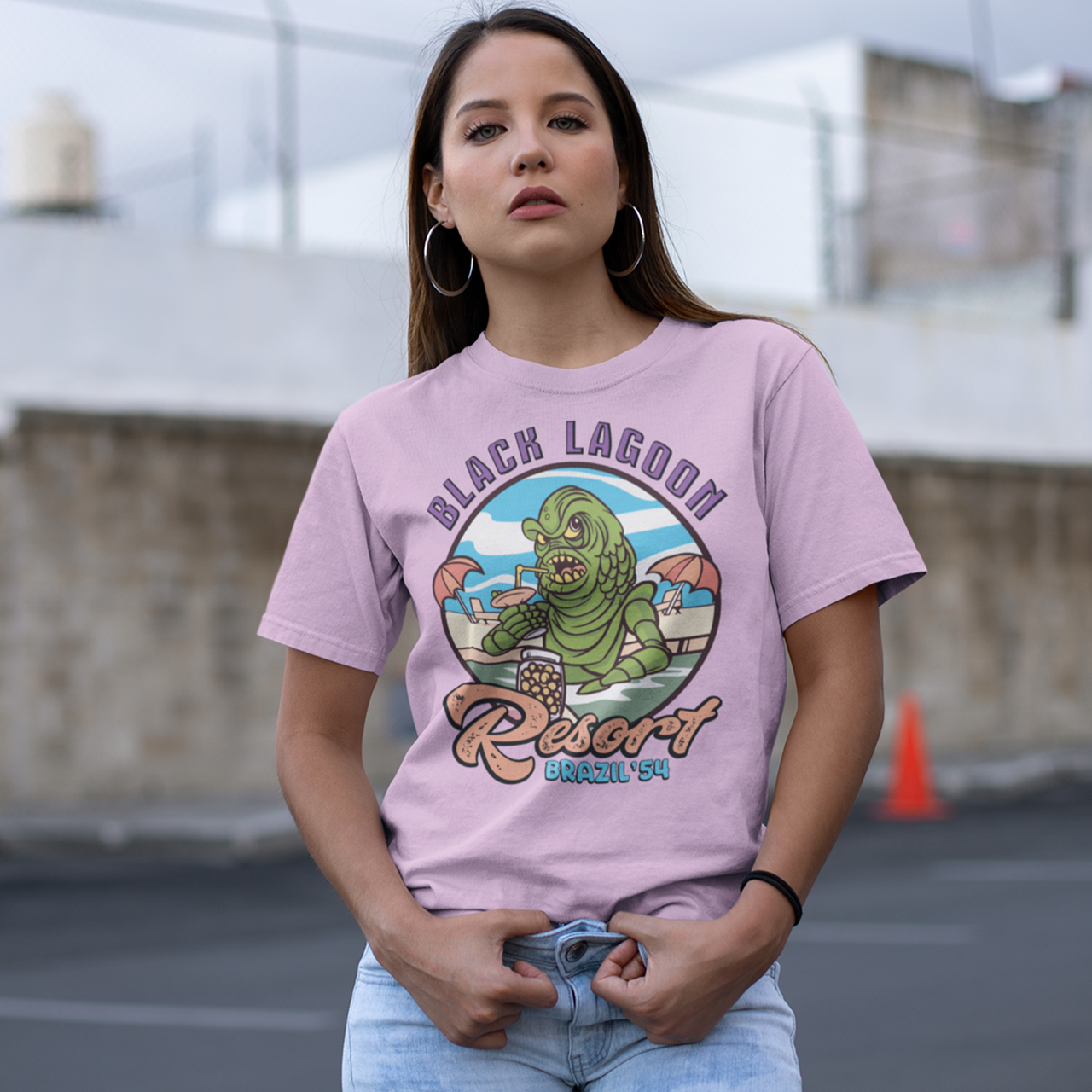 Pink t-shirt with the creature from the black lagoon drinking a cocktail in a pool with text "BLACK LAGOON RESORT".