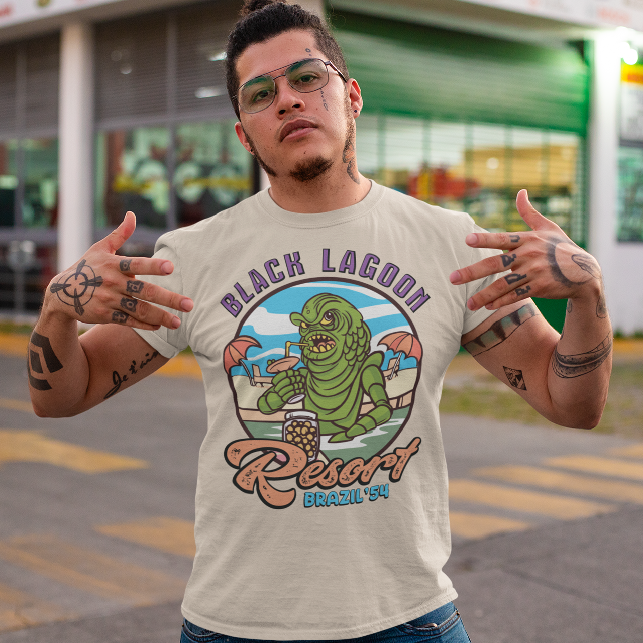 Cream t-shirt with the creature from the black lagoon drinking a cocktail in a pool with text "BLACK LAGOON RESORT".