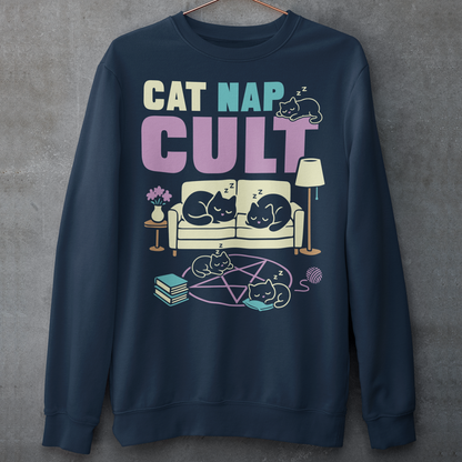 Navy sweatshirt with bold white text reading “Cat Nap Cult” above illustrations of sleeping cats lounging on a couch, books, and a pentagram-style ritual circle. The design includes cozy home details like a lamp, flowers, and yarn ball, creating a funny mix of occult humor and sleepy cat vibes in a minimalist monochrome style.