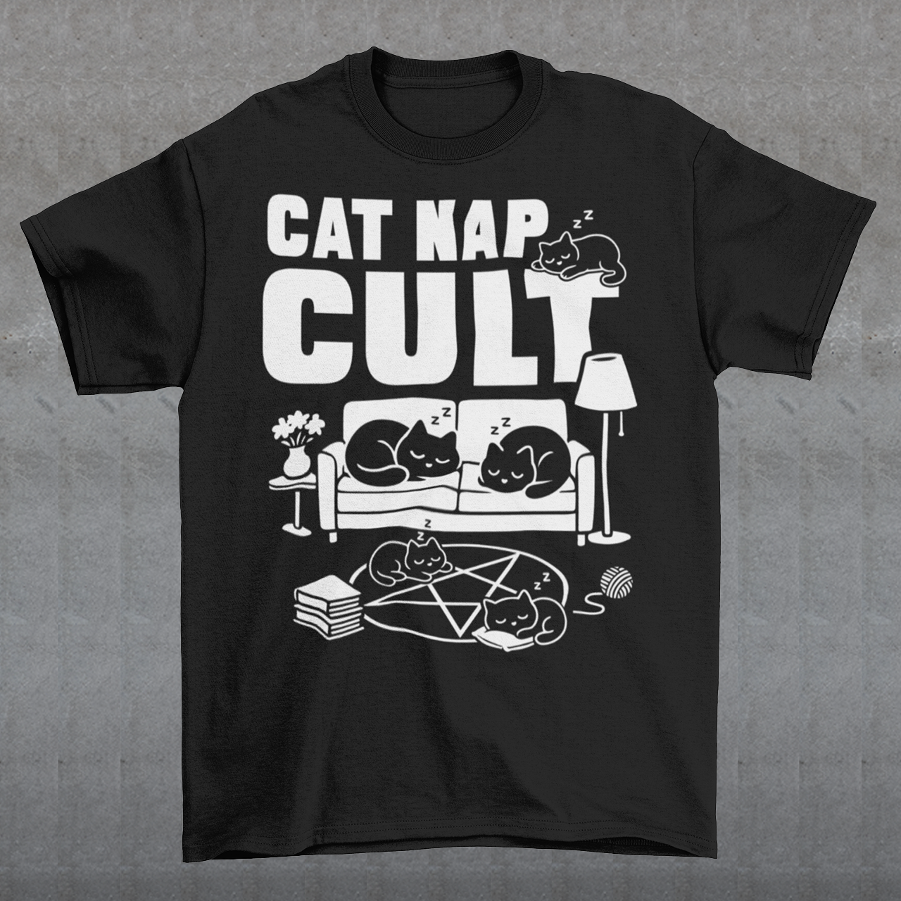 Black t-shirt with bold white text reading “Cat Nap Cult” above illustrations of sleeping cats lounging on a couch, books, and a pentagram-style ritual circle. The design includes cozy home details like a lamp, flowers, and yarn ball, creating a funny mix of occult humor and sleepy cat vibes in a minimalist monochrome style.