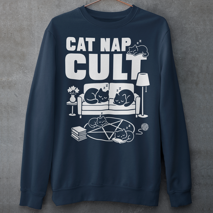 Navy sweatshirt with bold white text reading “Cat Nap Cult” above illustrations of sleeping cats lounging on a couch, books, and a pentagram-style ritual circle. The design includes cozy home details like a lamp, flowers, and yarn ball, creating a funny mix of occult humor and sleepy cat vibes in a minimalist monochrome style.