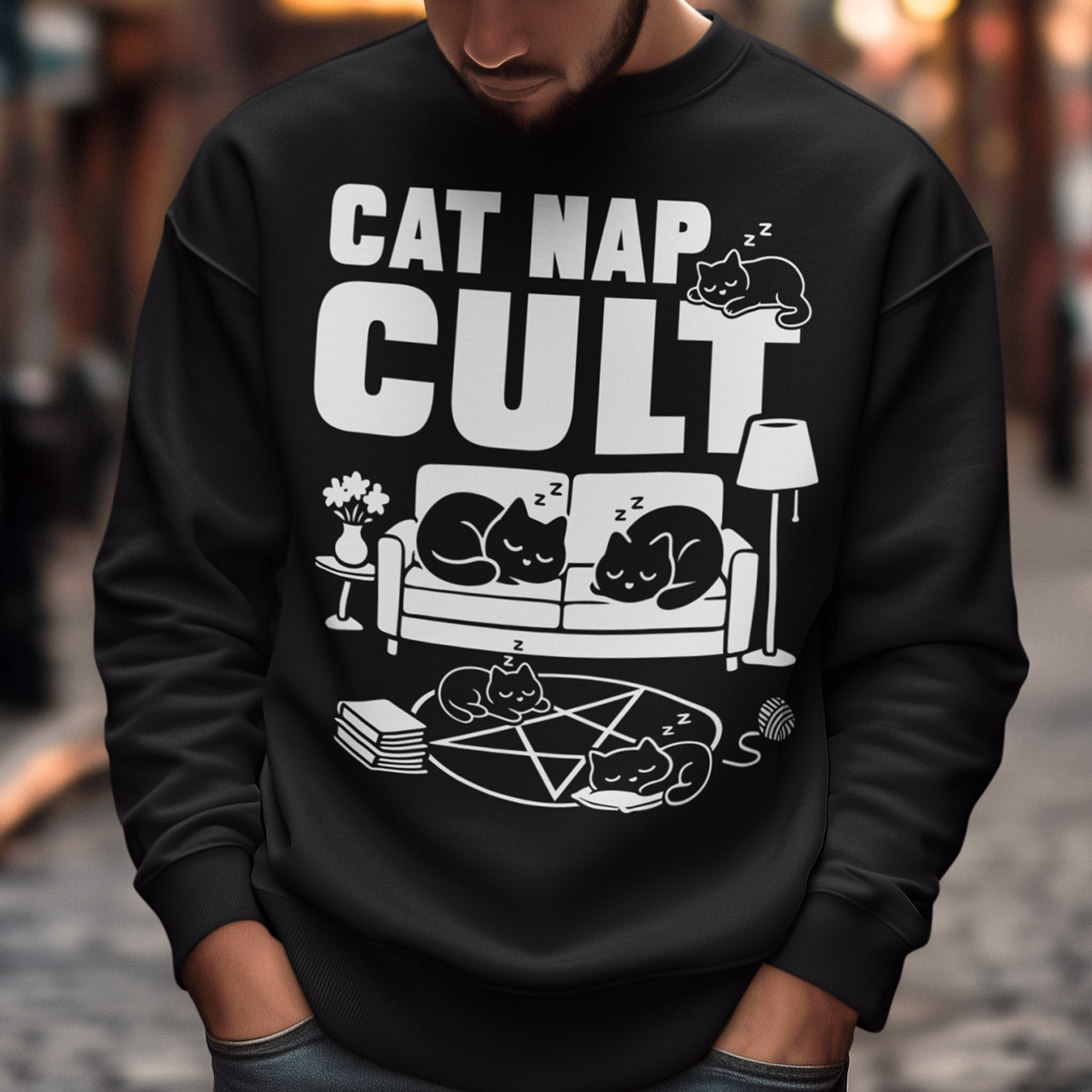 Black sweatshirt with bold white text reading “Cat Nap Cult” above illustrations of sleeping cats lounging on a couch, books, and a pentagram-style ritual circle. The design includes cozy home details like a lamp, flowers, and yarn ball, creating a funny mix of occult humor and sleepy cat vibes in a minimalist monochrome style.