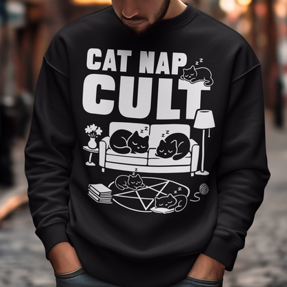 Black sweatshirt with bold white text reading “Cat Nap Cult” above illustrations of sleeping cats lounging on a couch, books, and a pentagram-style ritual circle. The design includes cozy home details like a lamp, flowers, and yarn ball, creating a funny mix of occult humor and sleepy cat vibes in a minimalist monochrome style.