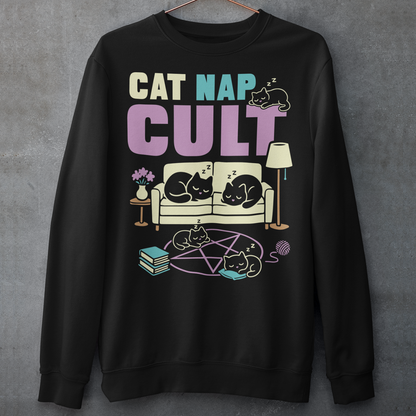 Black sweatshirt with bold white text reading “Cat Nap Cult” above illustrations of sleeping cats lounging on a couch, books, and a pentagram-style ritual circle. The design includes cozy home details like a lamp, flowers, and yarn ball, creating a funny mix of occult humor and sleepy cat vibes in a minimalist monochrome style.