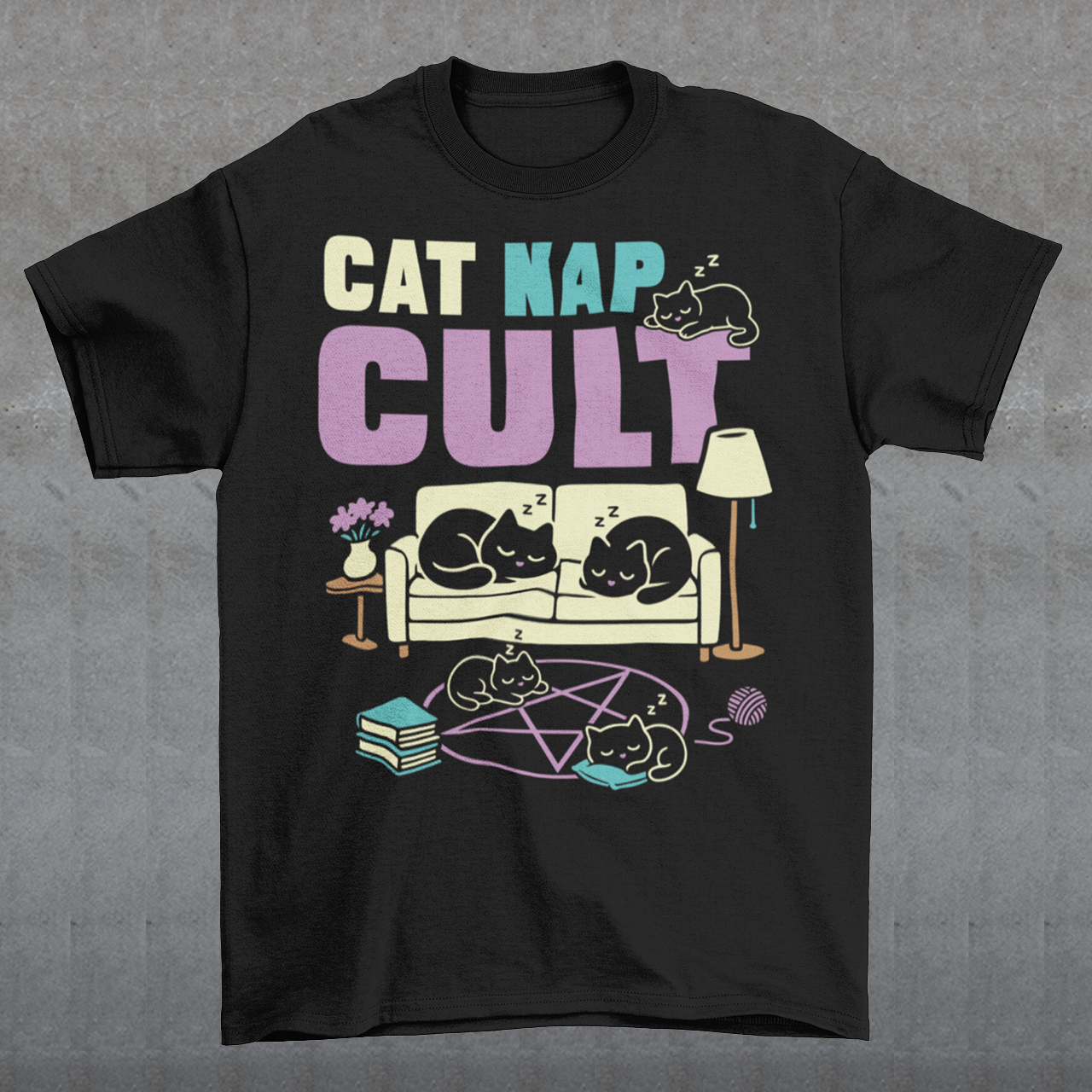 Black t-shirt with bold white text reading “Cat Nap Cult” above illustrations of sleeping cats lounging on a couch, books, and a pentagram-style ritual circle. The design includes cozy home details like a lamp, flowers, and yarn ball, creating a funny mix of occult humor and sleepy cat vibes in a minimalist monochrome style.