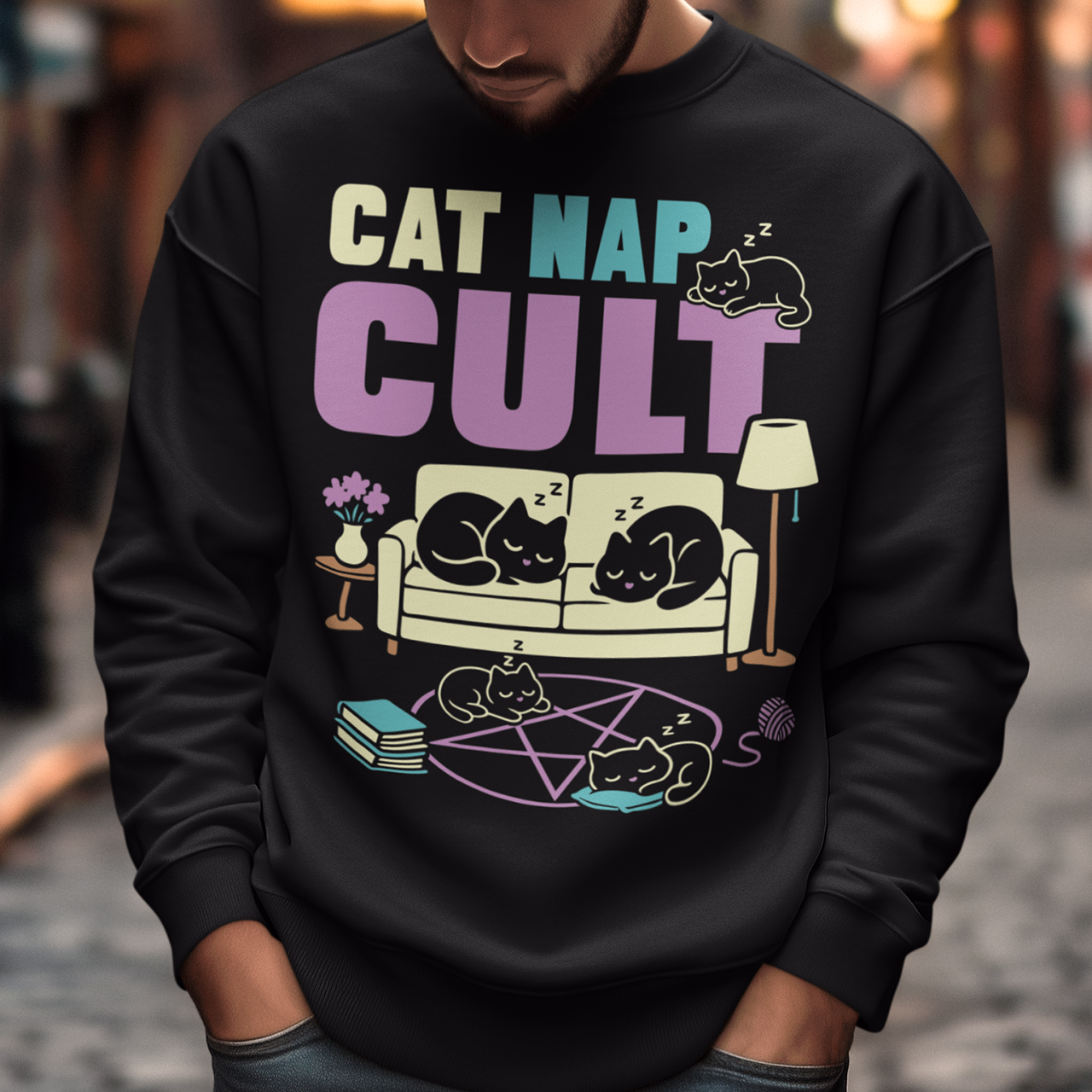 Black sweatshirt with bold white text reading “Cat Nap Cult” above illustrations of sleeping cats lounging on a couch, books, and a pentagram-style ritual circle. The design includes cozy home details like a lamp, flowers, and yarn ball, creating a funny mix of occult humor and sleepy cat vibes in a minimalist monochrome style.