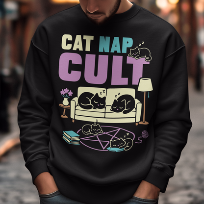 Black sweatshirt with bold white text reading “Cat Nap Cult” above illustrations of sleeping cats lounging on a couch, books, and a pentagram-style ritual circle. The design includes cozy home details like a lamp, flowers, and yarn ball, creating a funny mix of occult humor and sleepy cat vibes in a minimalist monochrome style.