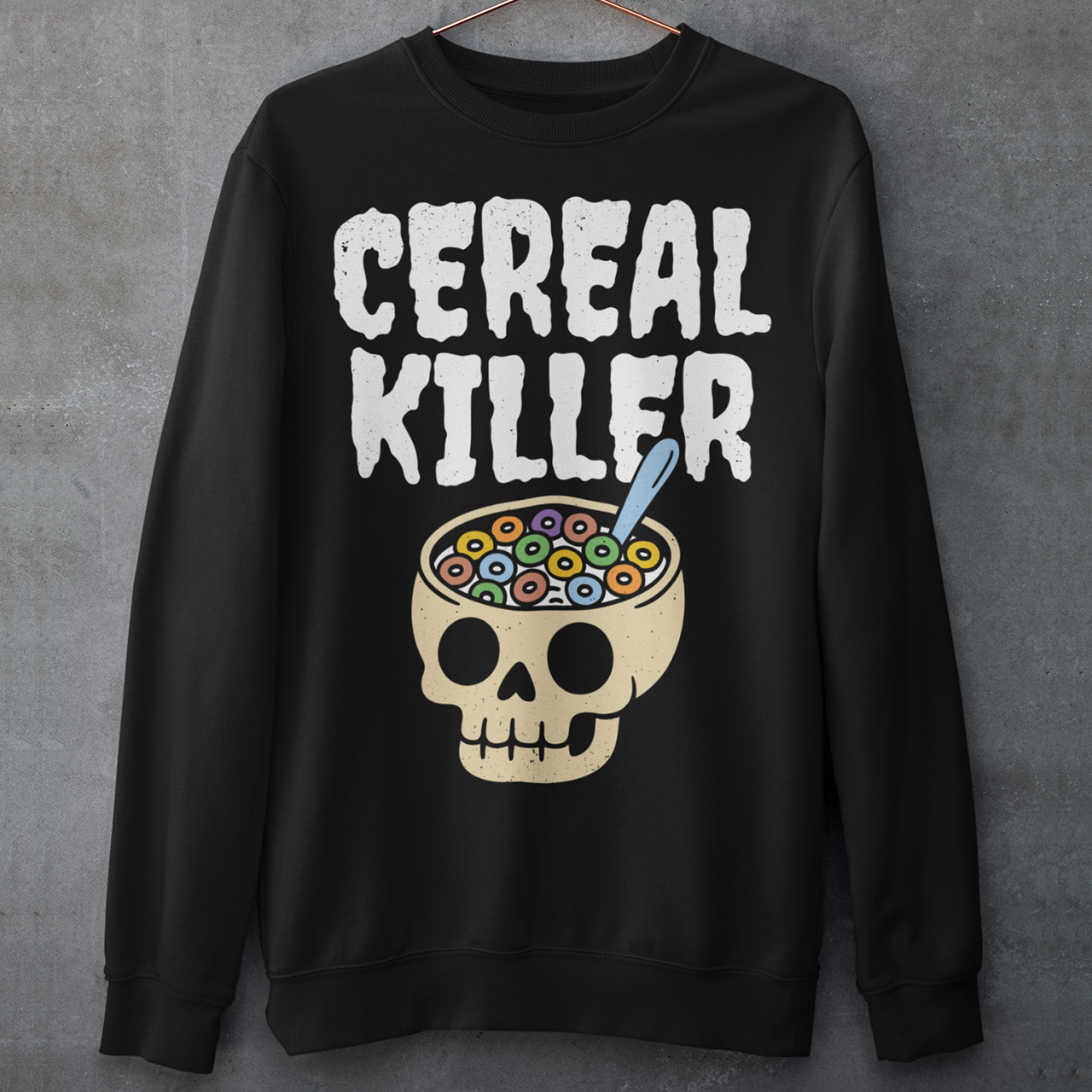 Black sweatshirt featuring the phrase “Cereal Killer” in large distressed white letters above a cartoon skull used as a cereal bowl filled with colorful cereal loops and a spoon. Funny dark humor design combining spooky Halloween style with breakfast pun humor.