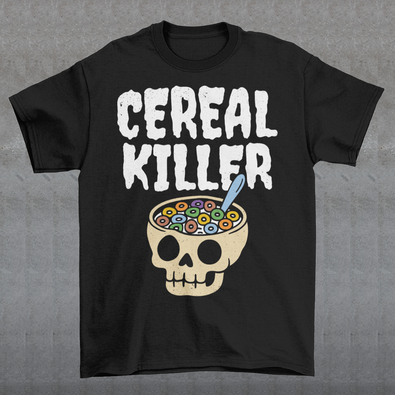 Black t-shirt featuring the phrase “Cereal Killer” in large distressed white letters above a cartoon skull used as a cereal bowl filled with colorful cereal loops and a spoon. Funny dark humor design combining spooky Halloween style with breakfast pun humor.