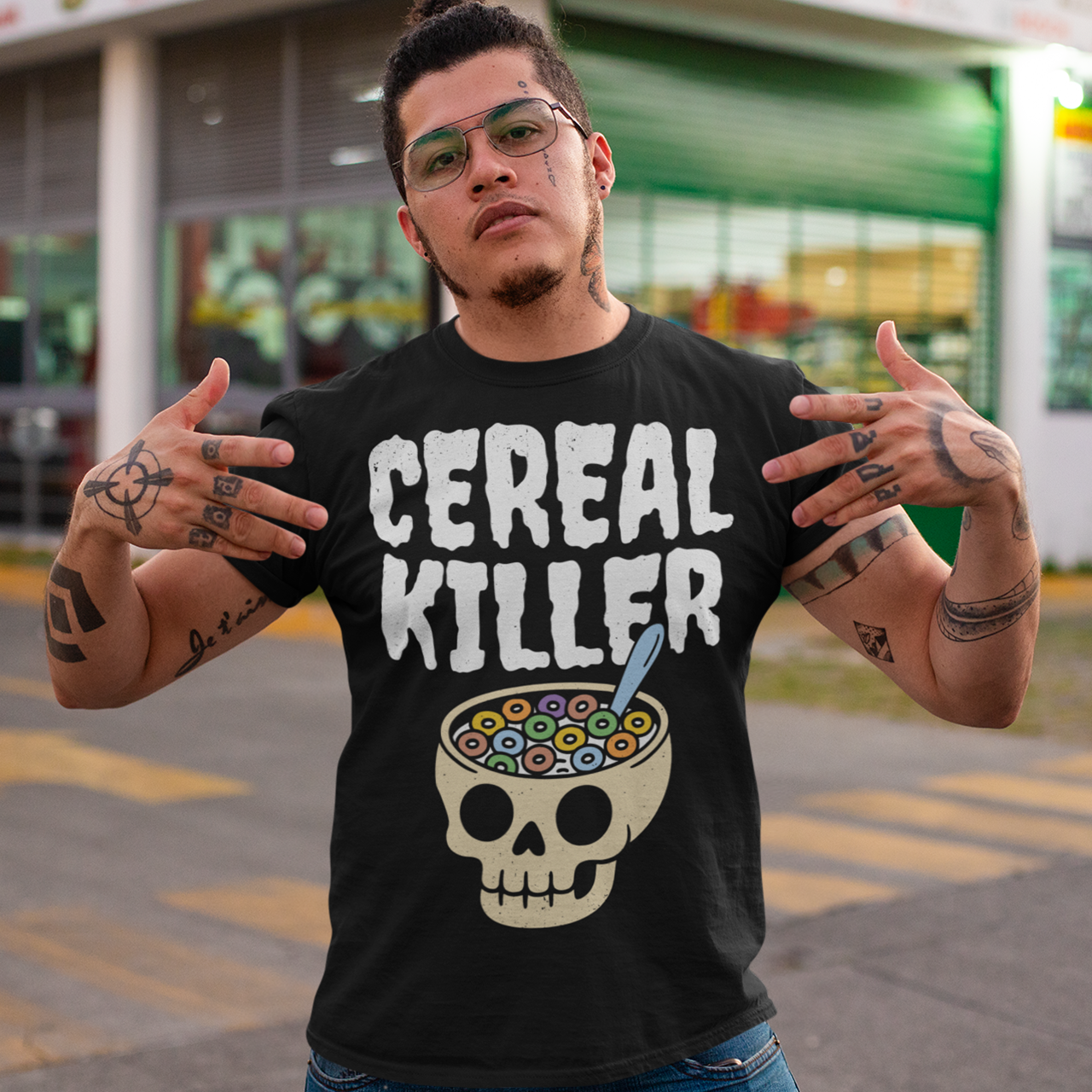 Black t-shirt featuring the phrase “Cereal Killer” in large distressed white letters above a cartoon skull used as a cereal bowl filled with colorful cereal loops and a spoon. Funny dark humor design combining spooky Halloween style with breakfast pun humor.