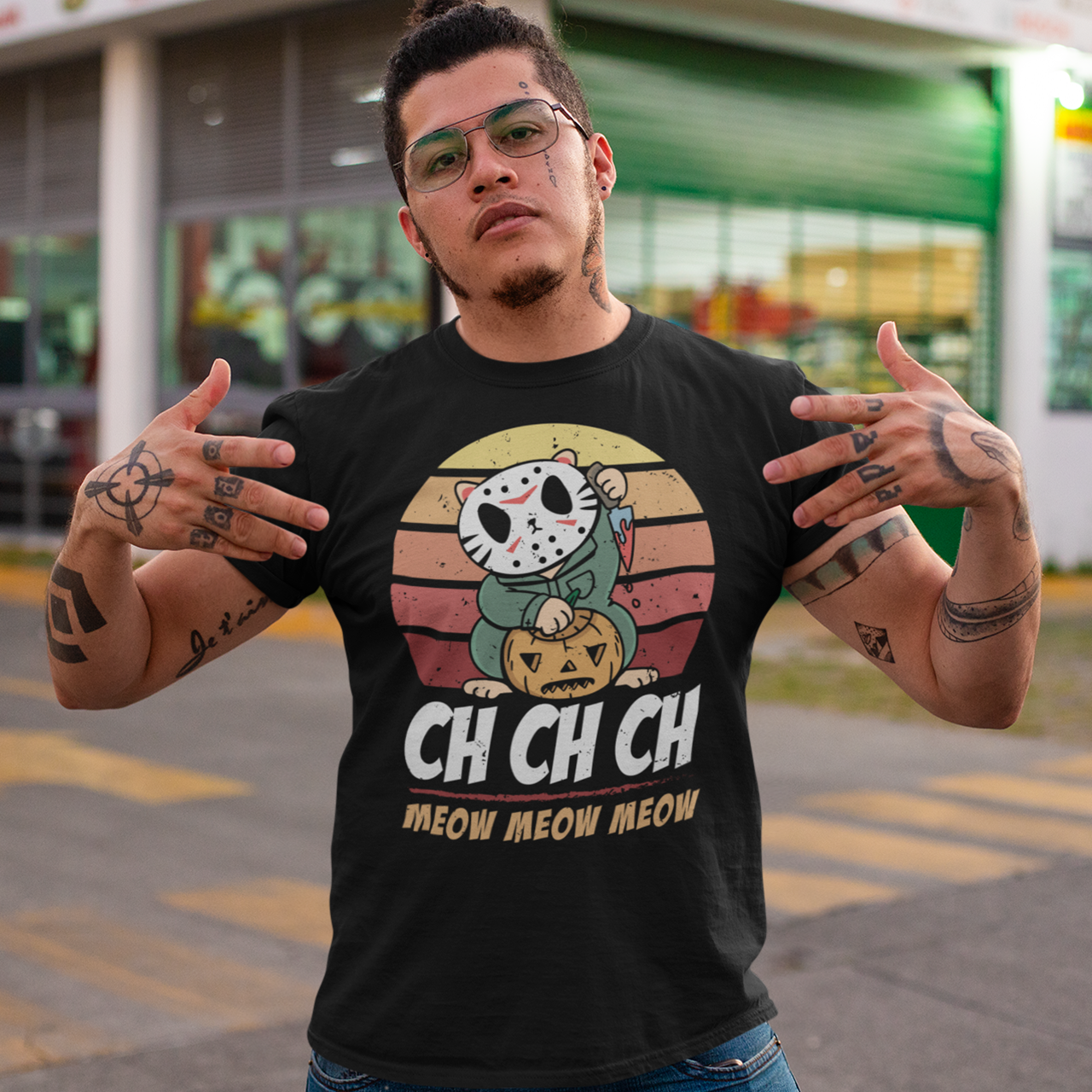 Black halloween t-shirt of a cat in a horror costume with retro sun background with text underneath  "CH CH CH MEOW MEOW MEOW".