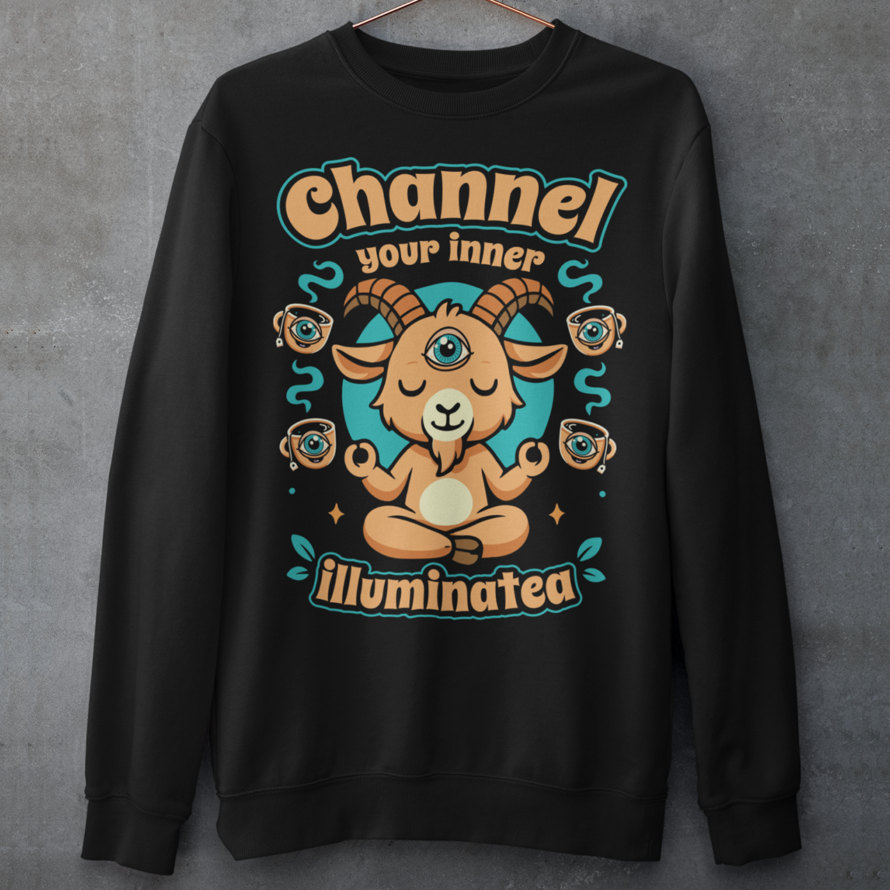 Black t-shirt featuring a humorous occult-inspired design with the text “Channel Your Inner Illuminatea.” The artwork shows a meditating goat with a third eye, crossed legs, and raised hands, surrounded by floating teacups decorated with all-seeing eyes. Teal and tan accents create a mystical aesthetic blending spiritual symbolism, conspiracy humor, meditation themes, and playful occult artwork. Perfect for fans of witchy, esoteric, and funny graphic tees.