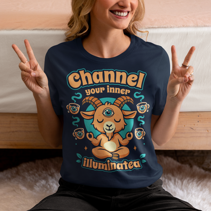 Navy t-shirt featuring a humorous occult-inspired design with the text “Channel Your Inner Illuminatea.” The artwork shows a meditating goat with a third eye, crossed legs, and raised hands, surrounded by floating teacups decorated with all-seeing eyes. Teal and tan accents create a mystical aesthetic blending spiritual symbolism, conspiracy humor, meditation themes, and playful occult artwork. Perfect for fans of witchy, esoteric, and funny graphic tees.