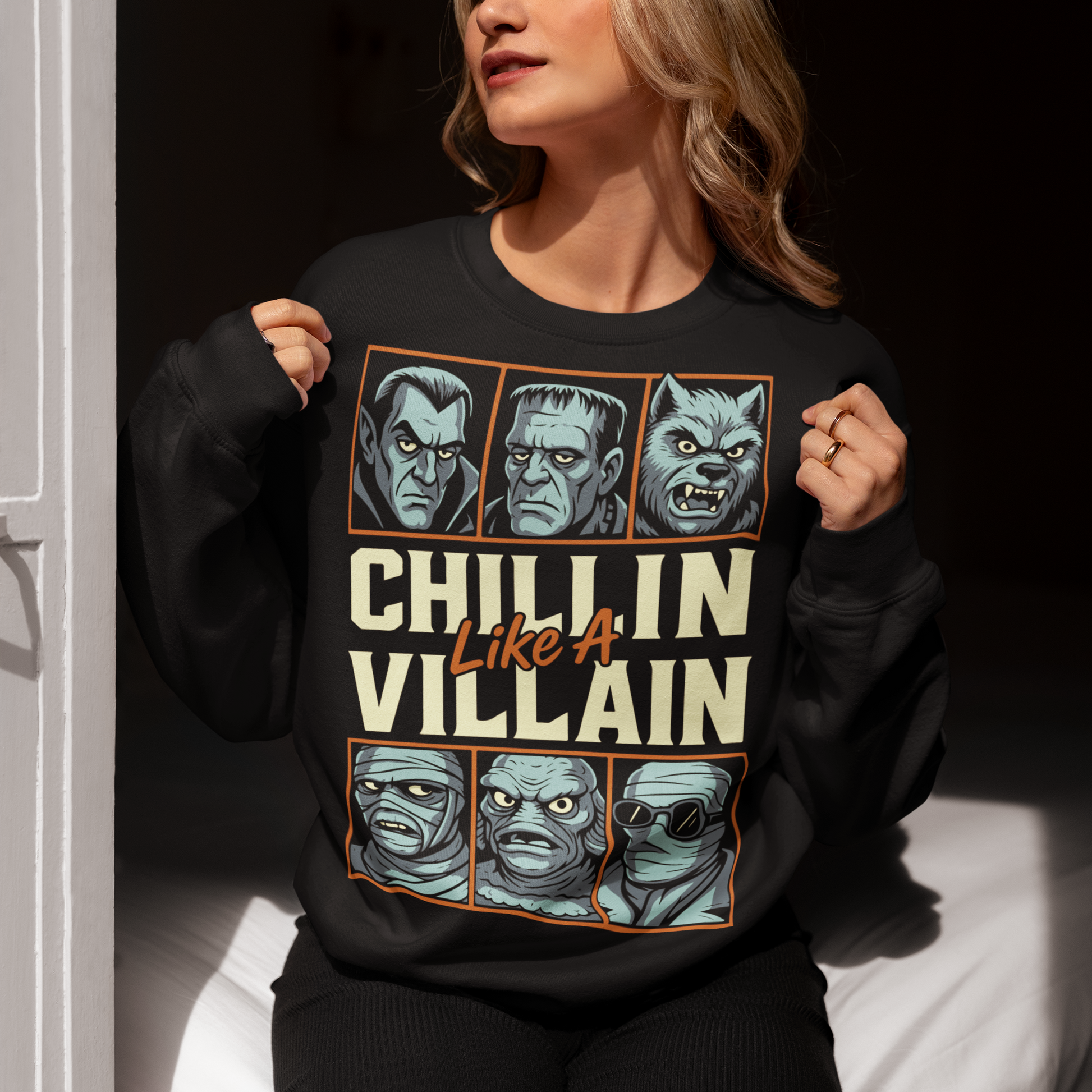 Black sweatshirt featuring the phrase "Chillin Like A Villain" with six classic horror monster portraits, including a vampire, Frankenstein's monster, werewolf, mummy, swamp creature, and the Invisible Man. The retro-inspired graphic uses distressed vintage styling with bold cream and orange lettering, making it a fun horror-themed shirt for Halloween, monster movie fans, goth fashion lovers, and classic horror enthusiasts.
