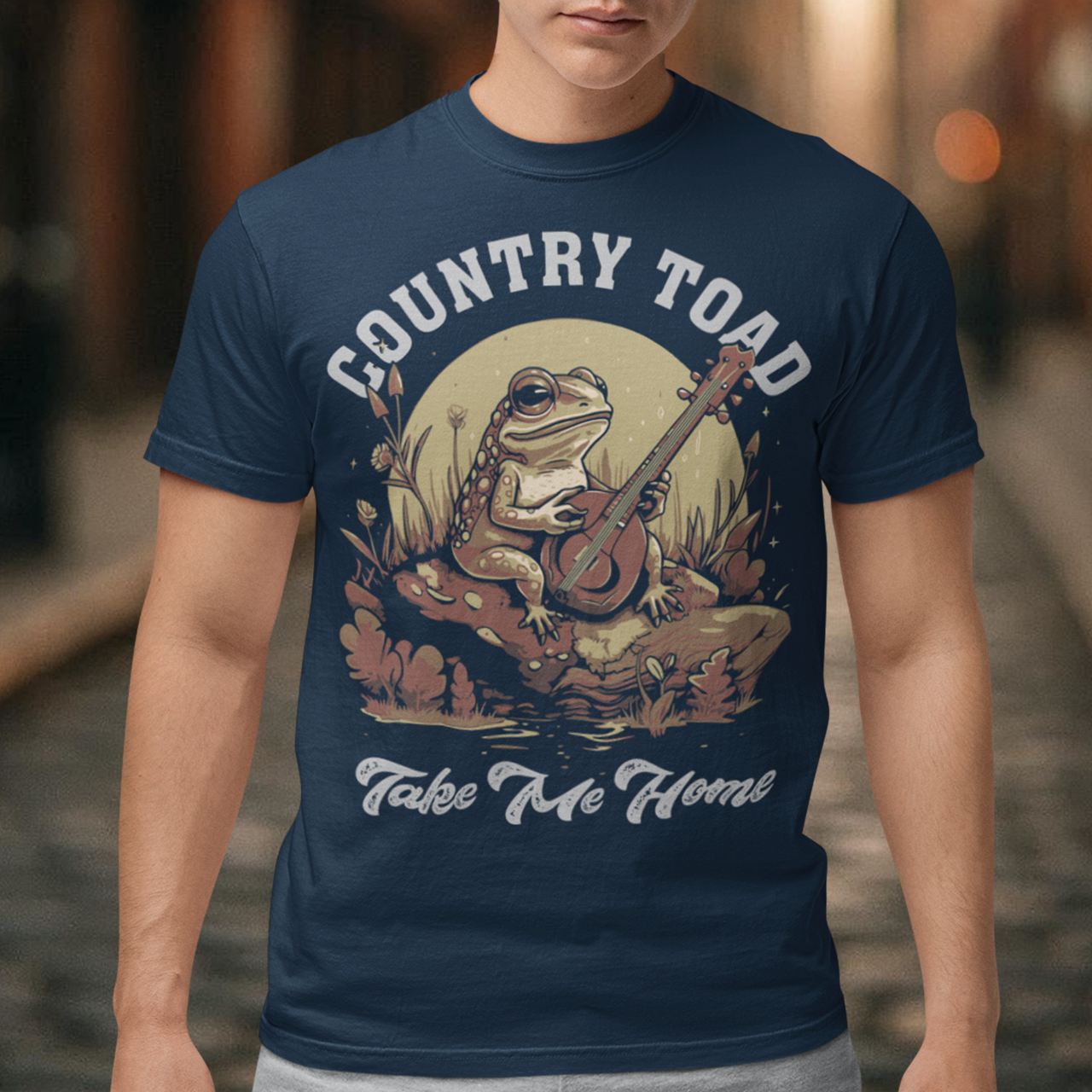 Introducing our delightful "Country Toad Take Me Home" t-shirt, where whimsy and charm come together in perfect harmony. This enchanting design captures the essence of a peaceful evening in the countryside, transporting you to a world where nature and music blend seamlessly. At the center of the design, you'll find a vibrant depiction of a serene pond illuminated by the gentle glow of the moon. Resting on a moss-covered rock, a plucky frog musician steals the show as it strums a banjo.